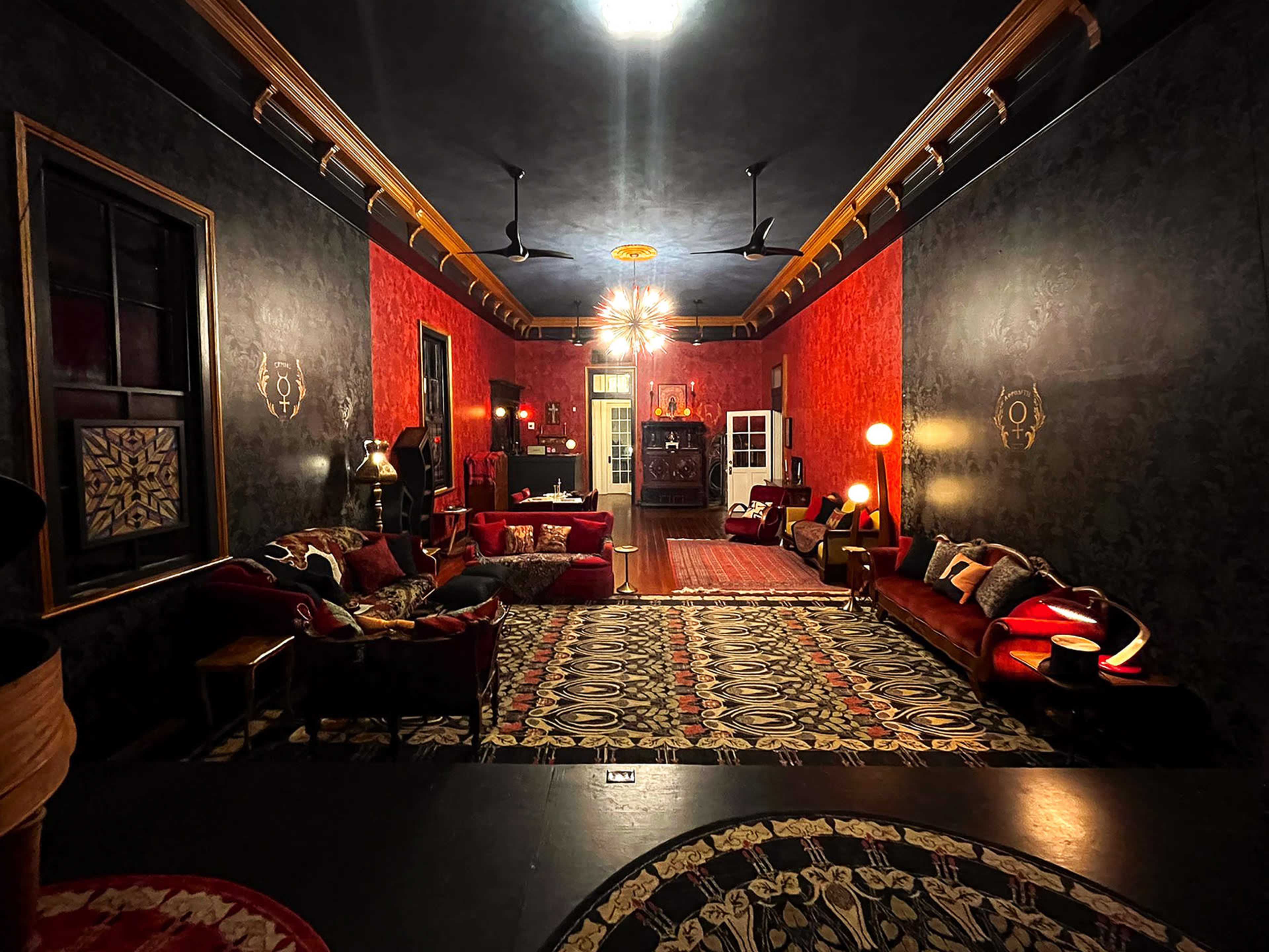 The image depicts a dimly lit lounge with red and black walls, featuring ornate furniture and decorative lighting.
