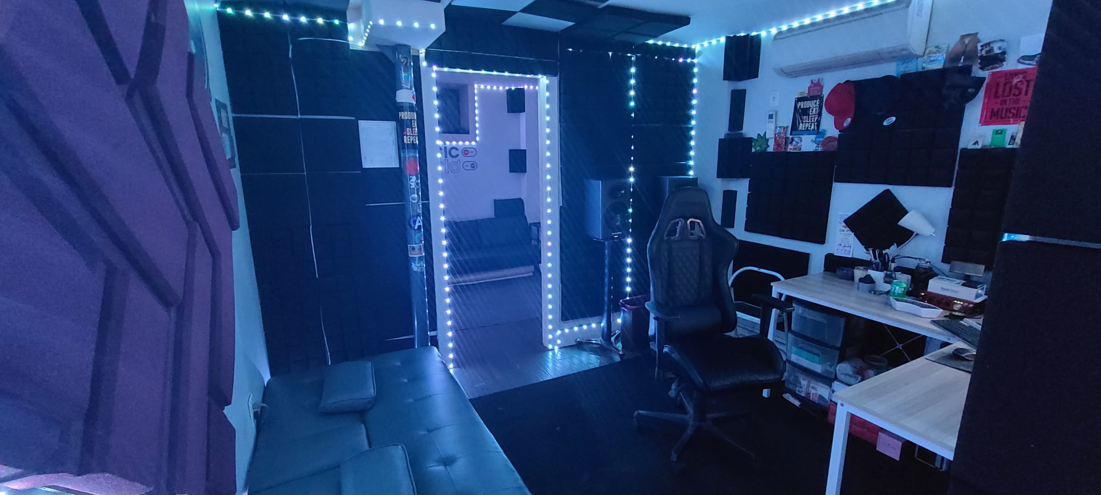 A soundproofed room with black acoustic panels, a lounge area with a sofa, and a desk with an office chair, all illuminated by LED lights.