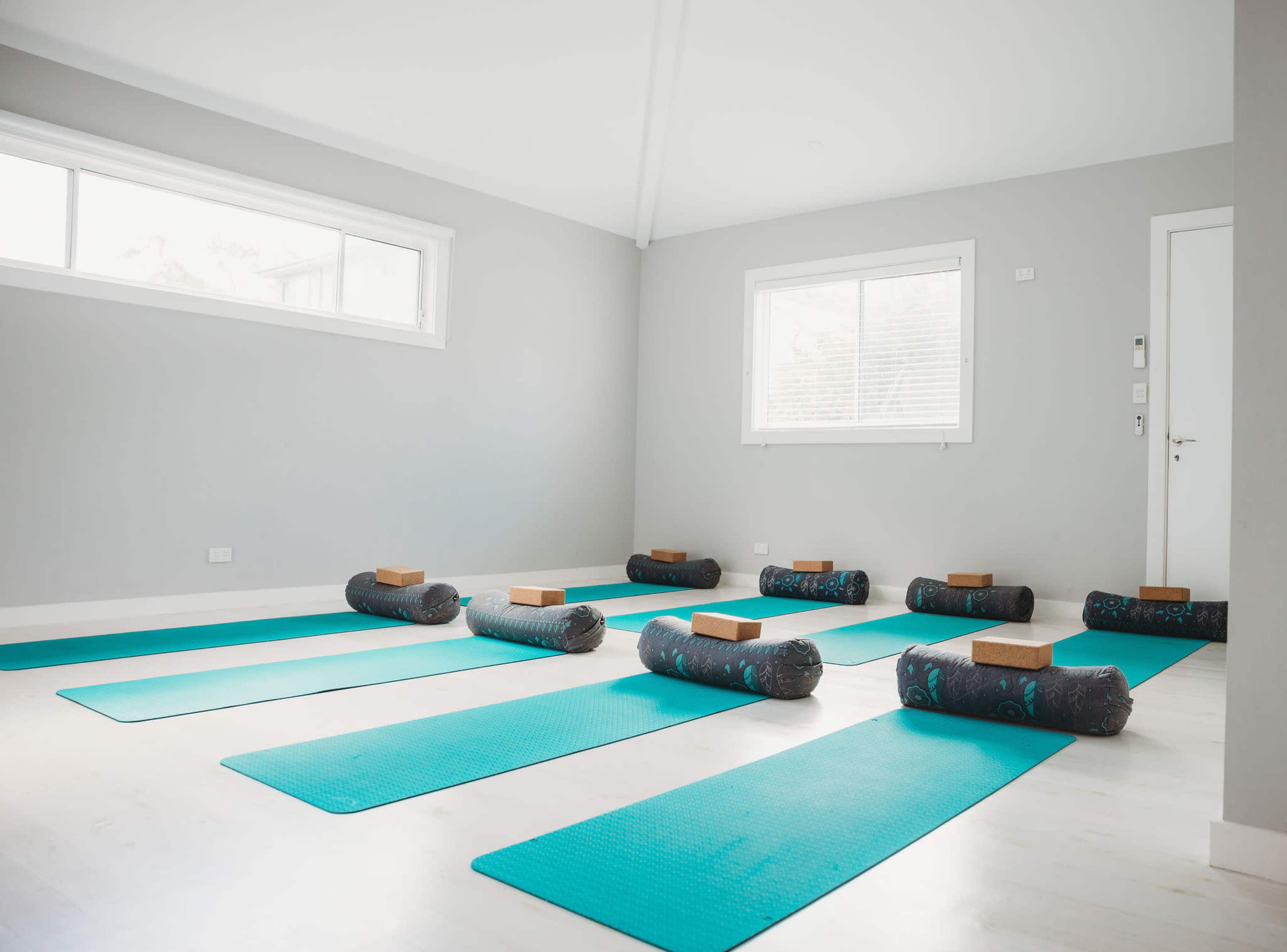 A yoga studio with several blue mats arranged on the floor, each topped with a bolster and block.