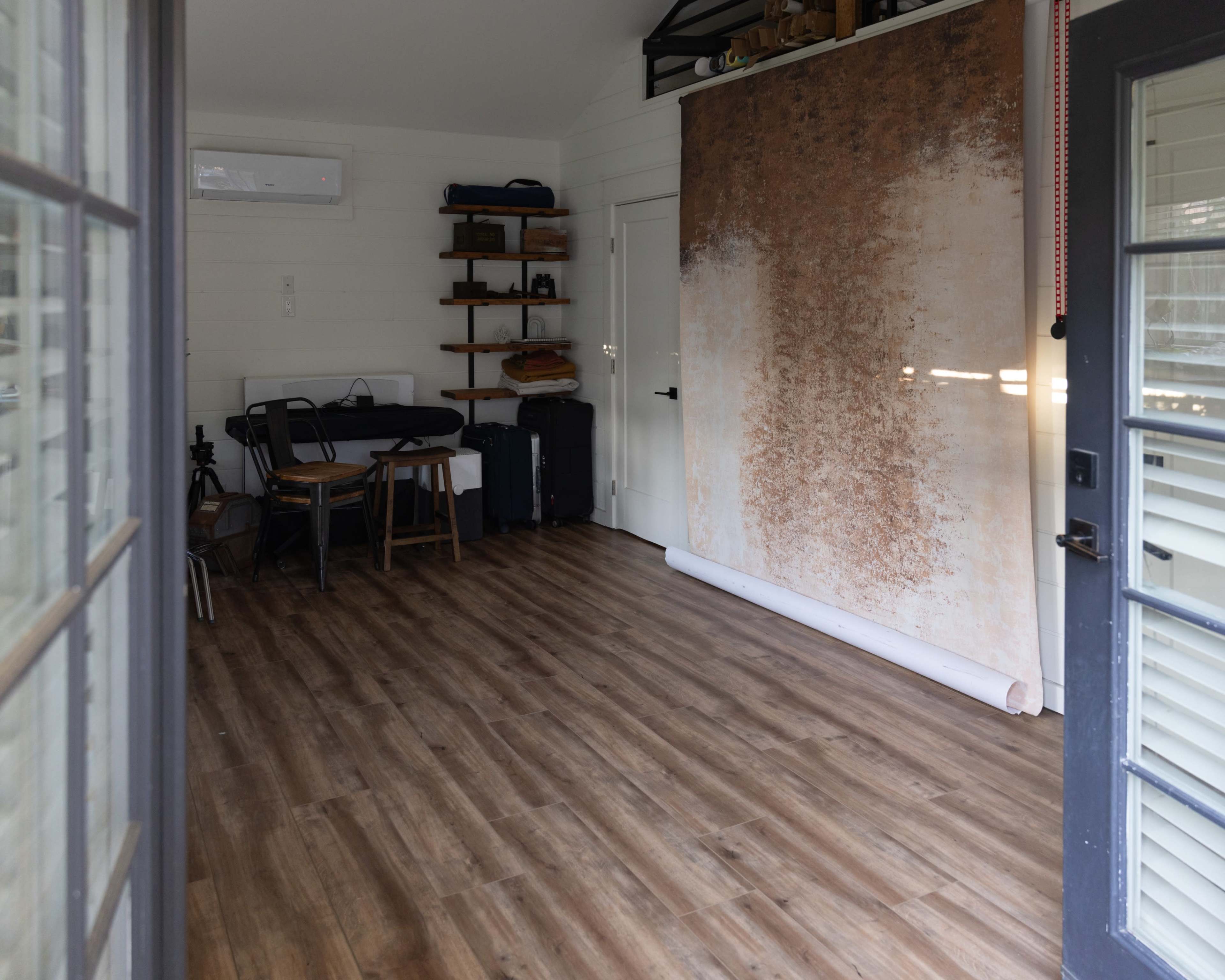 The room features a wooden floor, a large backdrop against one wall, a table with chairs, and various storage items along the shelves.