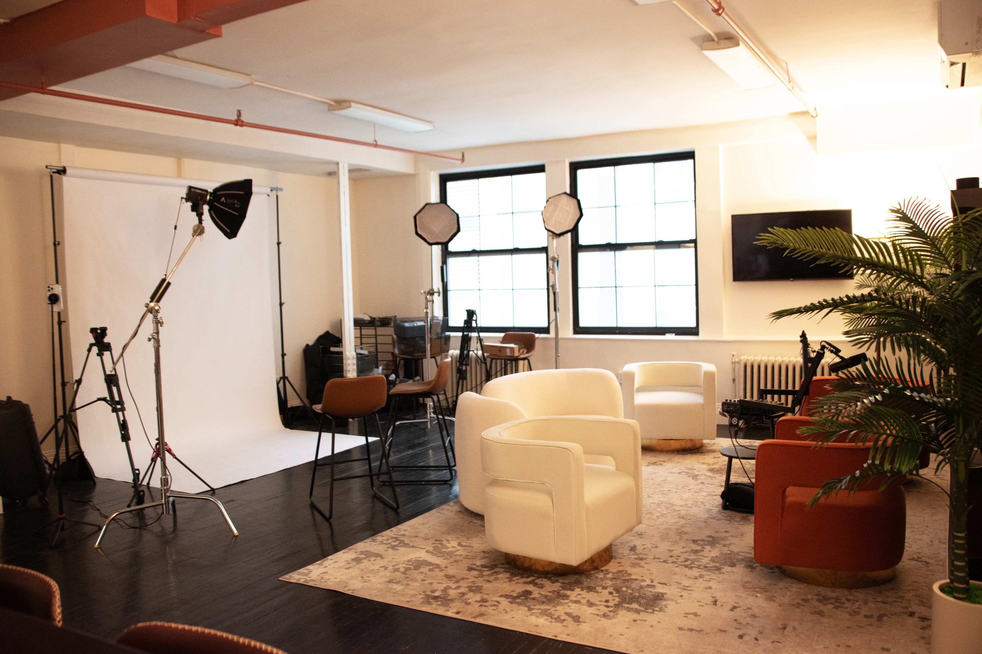 The image shows a spacious studio with various seating arrangements, photography equipment, and a large backdrop setup.