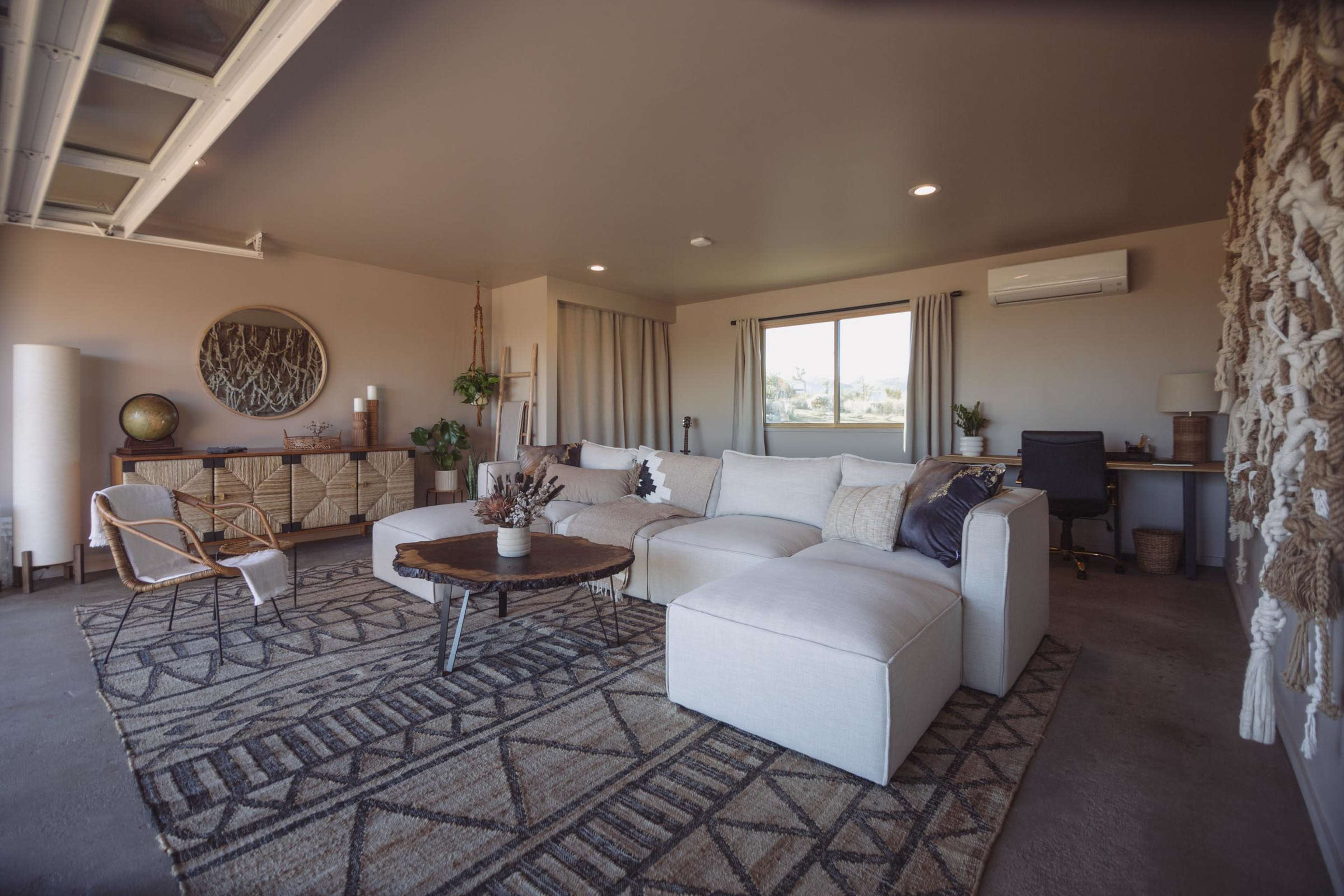 A modern living room with a sectional sofa, a coffee table, a patterned rug, and a mix of decorative plants and furniture.
