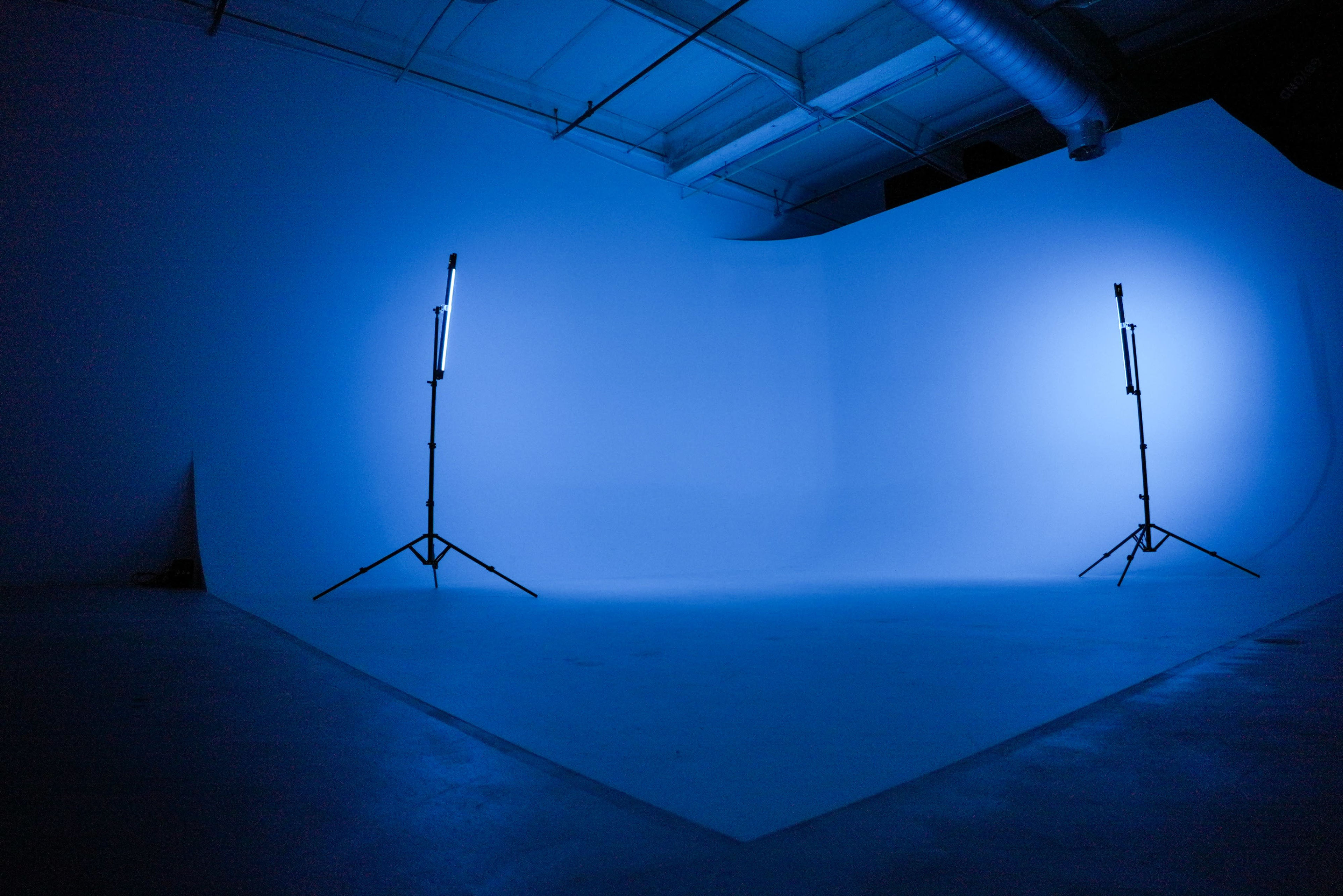 A photo studio with a blank backdrop illuminated by two blue stage lights on stands.