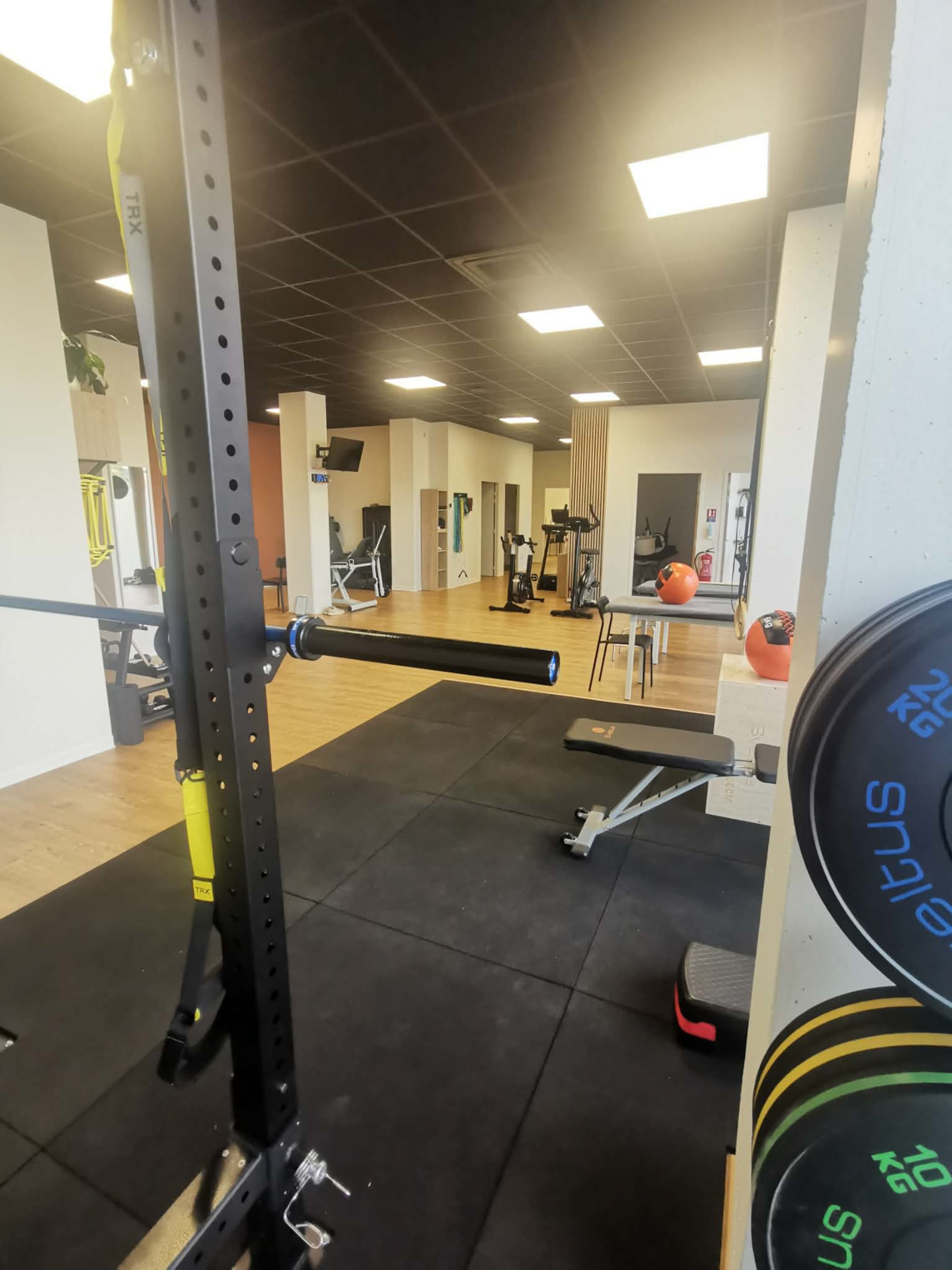 The image shows a well-equipped gym with various exercise machines and weightlifting equipment arranged neatly on a rubber floor.