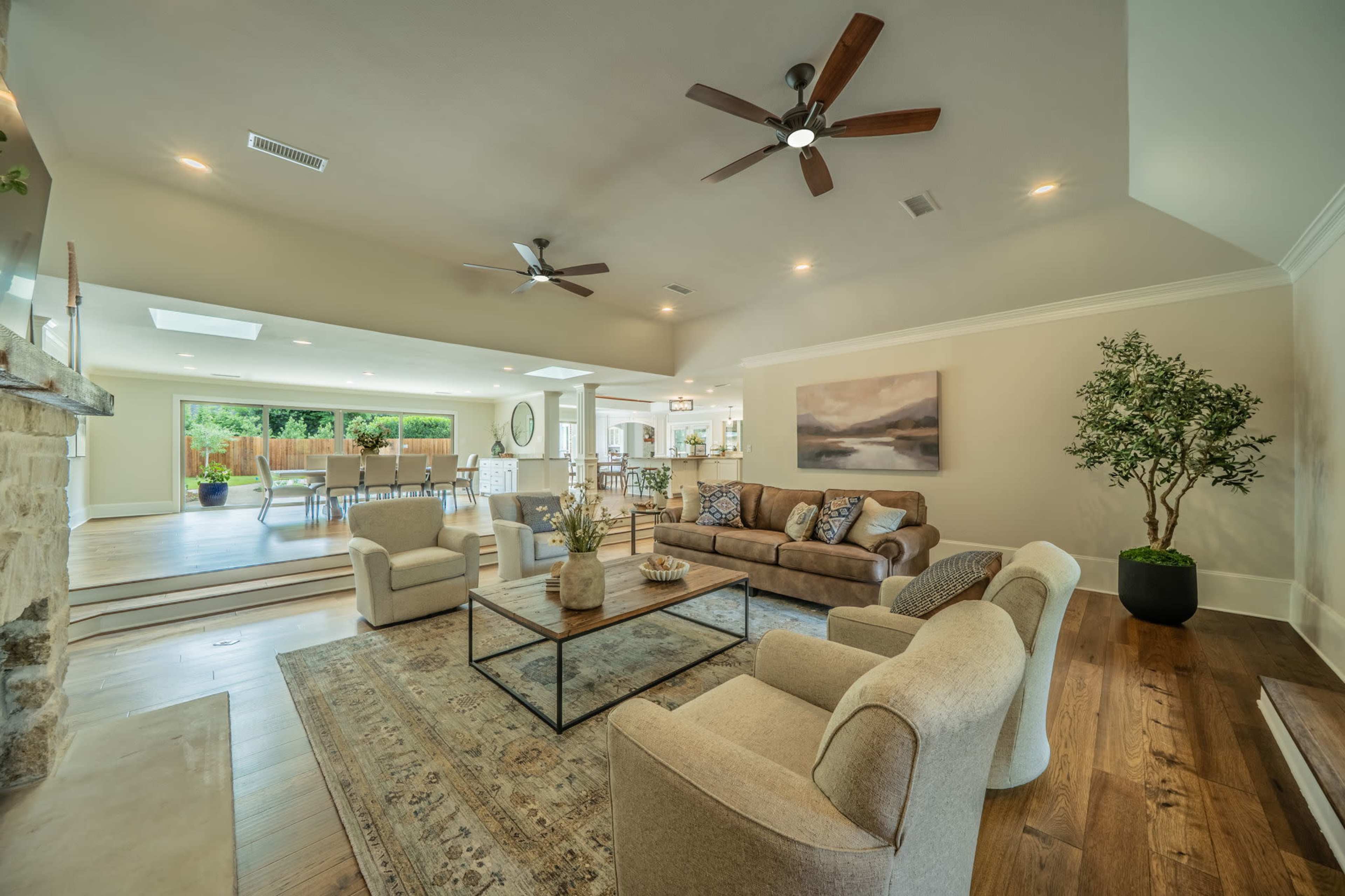 The image shows a spacious living room with a sectional sofa, two armchairs, a coffee table, and large windows that lead to an outdoor area.