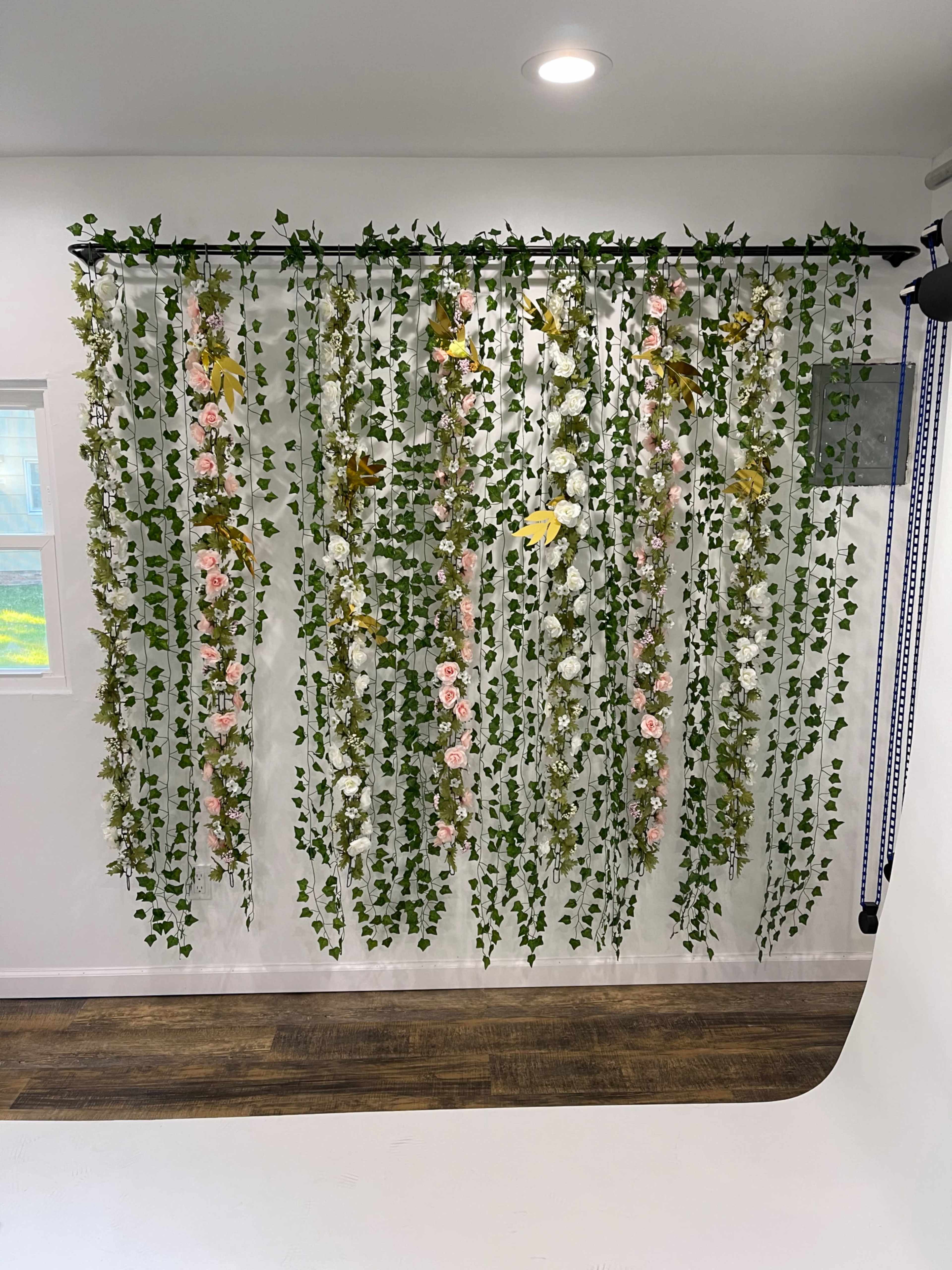 A wall adorned with cascading artificial flowers and greenery hangs from a supporting structure in a well-lit room.