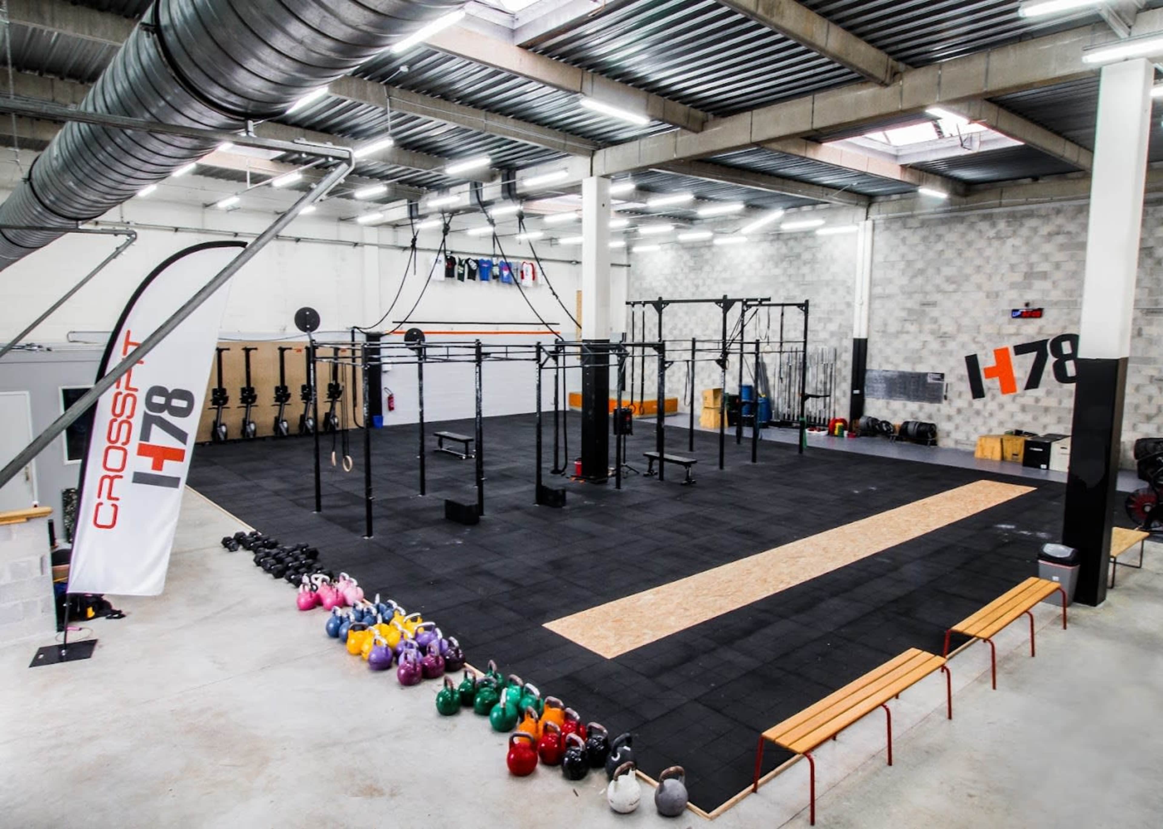 A spacious gym area equipped with various workout stations, kettlebells arranged along one side, and a large open floor for exercises.