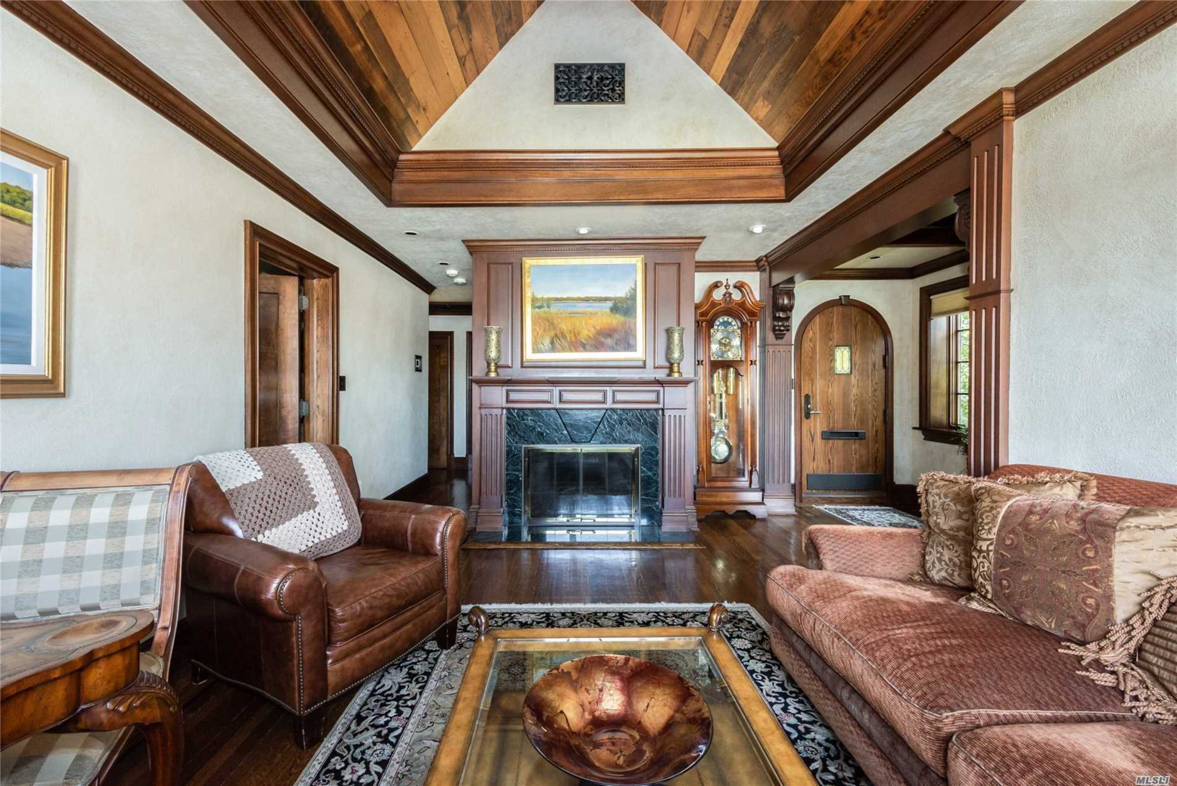 A cozy living room with a fireplace, wooden ceiling, and a mix of leather and upholstered furniture.