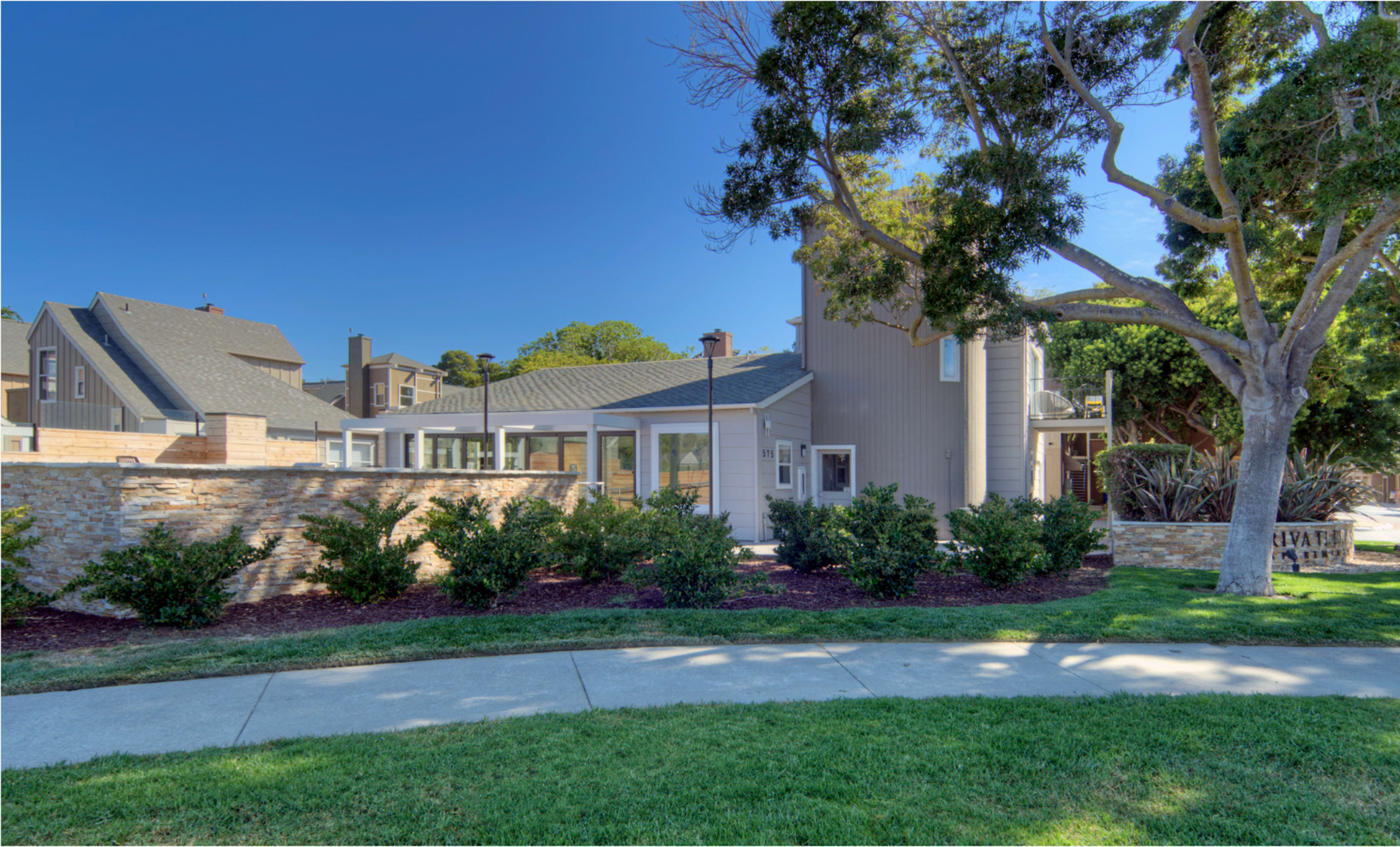 The image shows a modern house with a landscaped yard, situated near a sidewalk in a residential neighborhood.