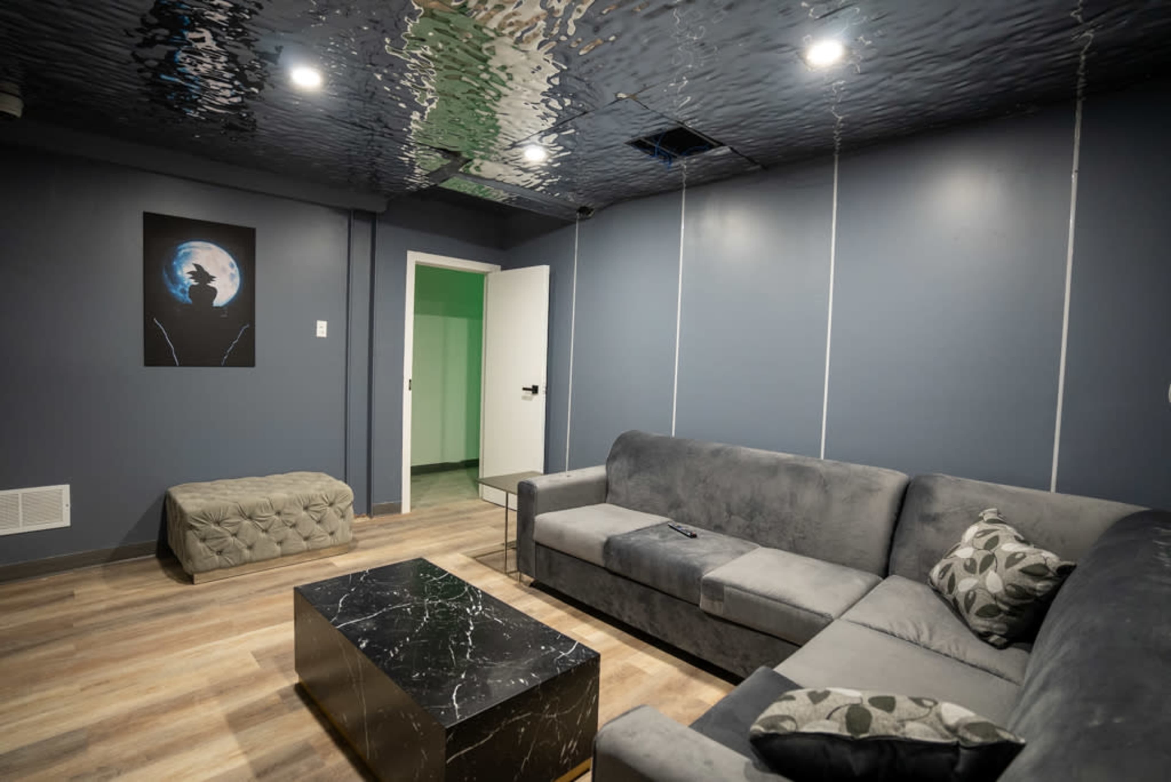 A modern living room featuring a gray sectional sofa, a black marble coffee table, and a ceiling that reflects light with a wavy appearance.
