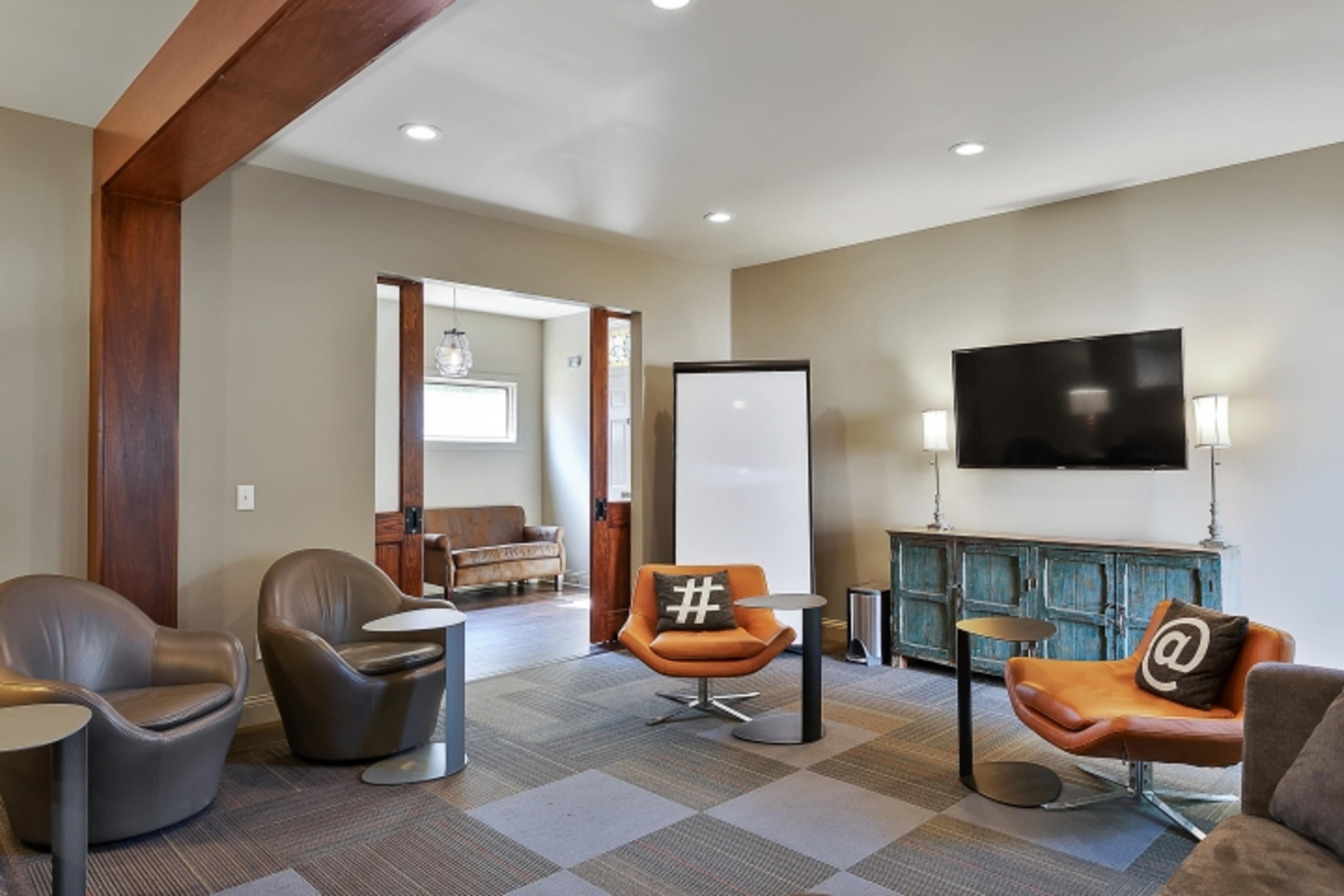 A modern lounge area with two chairs featuring symbols, a television mounted on the wall, and a doorway leading to another room.