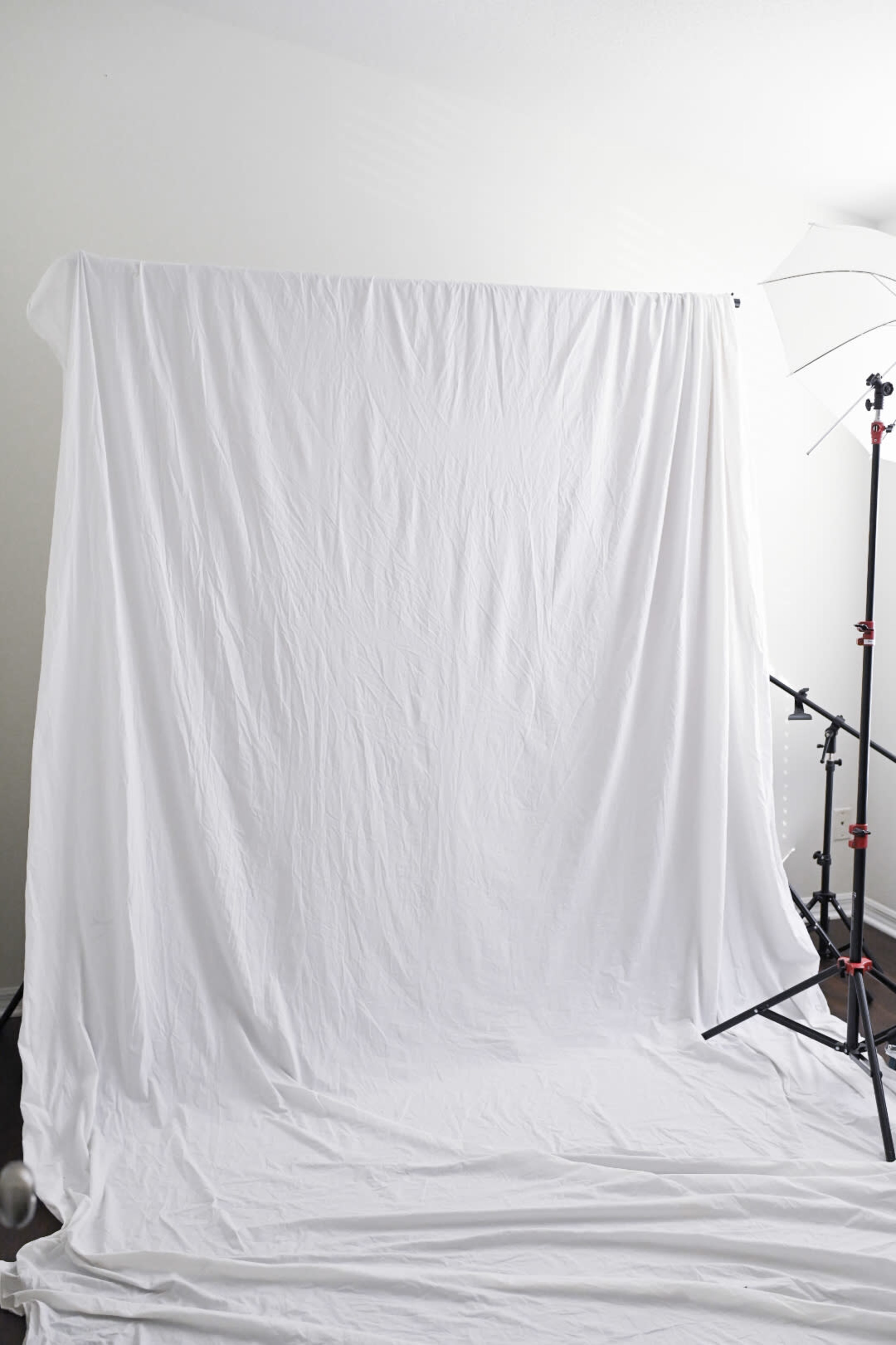 The image shows a photography studio setup with a large white backdrop and a light stand.
