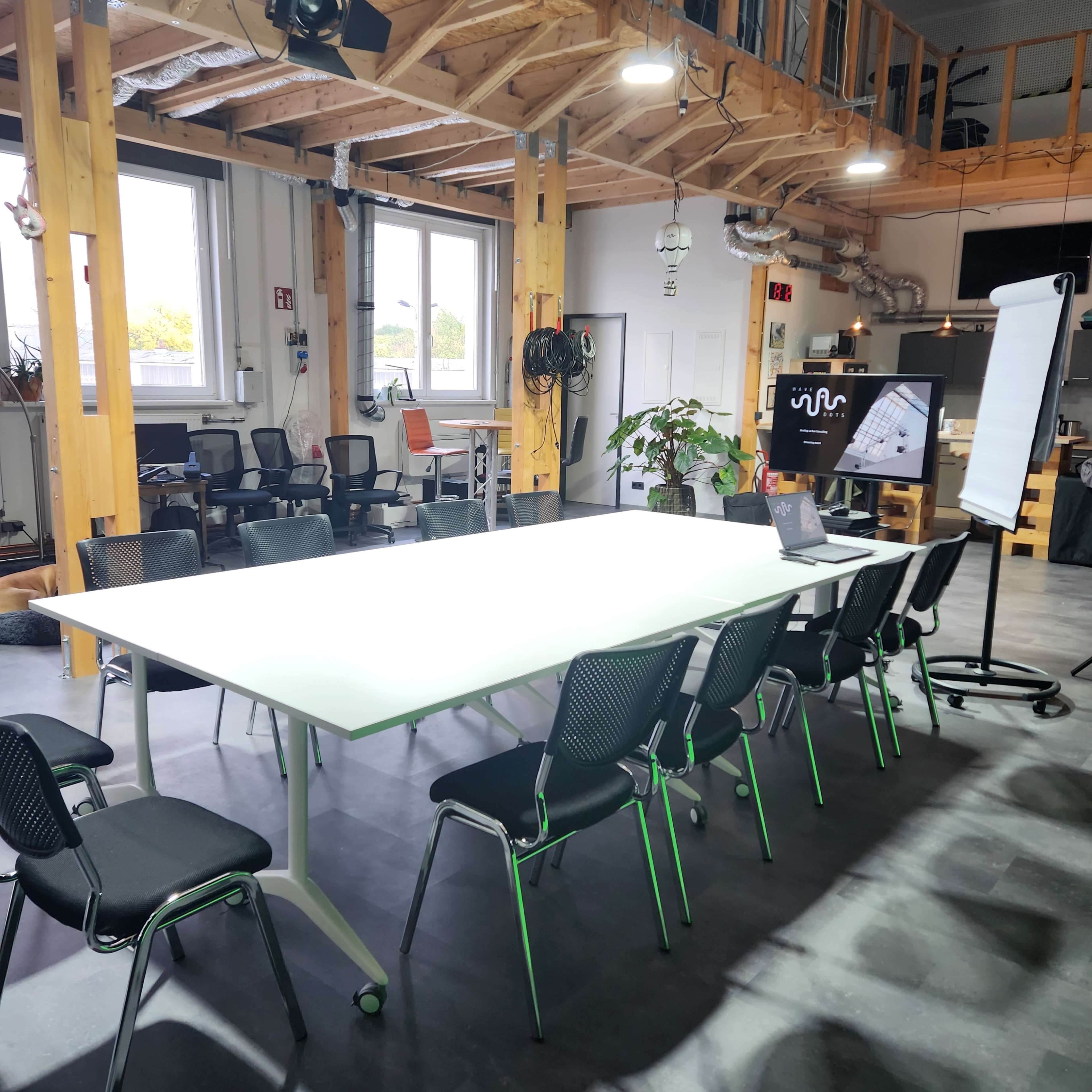 The image shows a modern conference room with a large white table surrounded by black chairs, a projector screen displaying a presentation, and a flip chart stand.