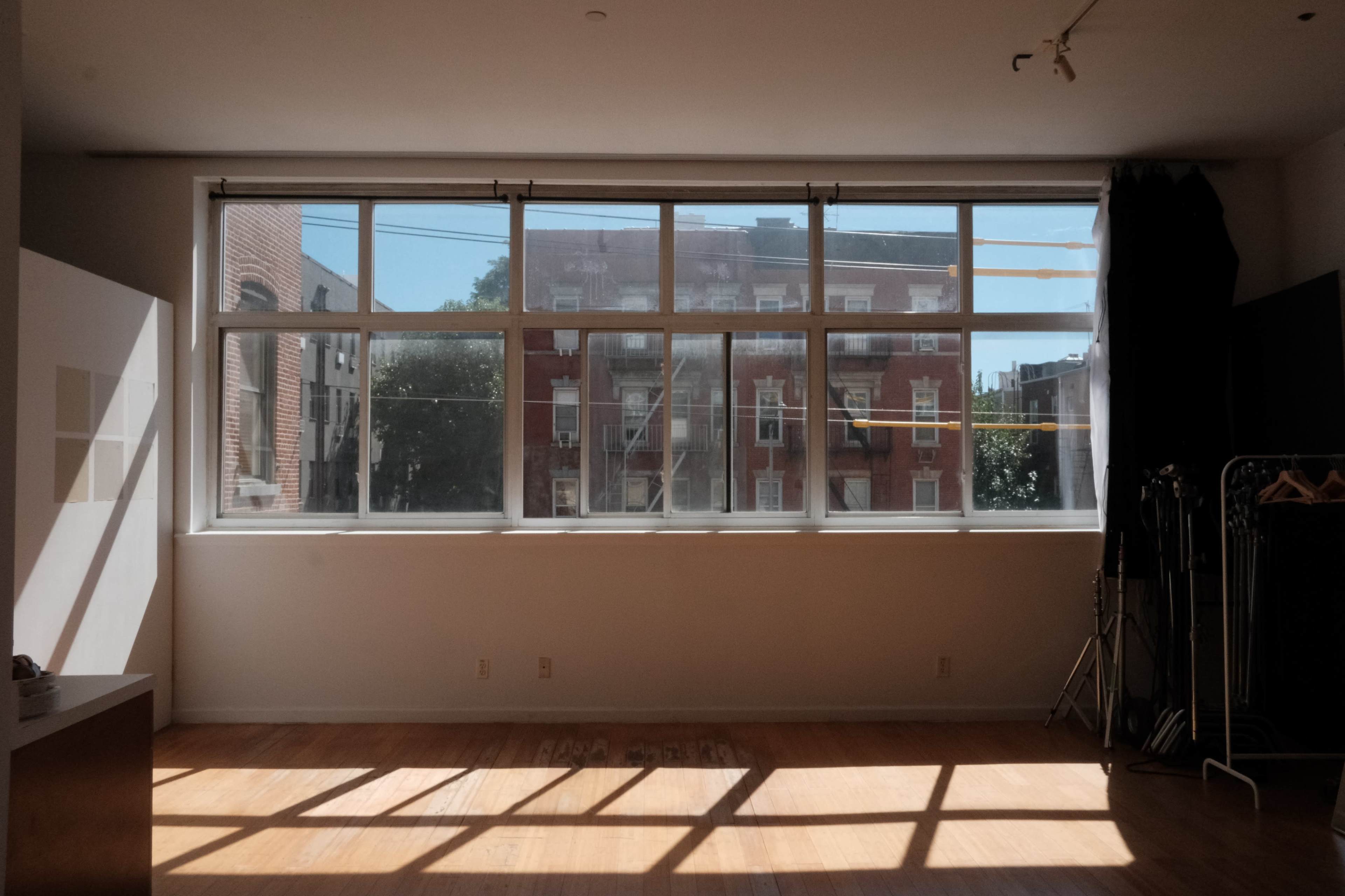A bright, empty room with large windows overlooking a brick building and wooden floors.