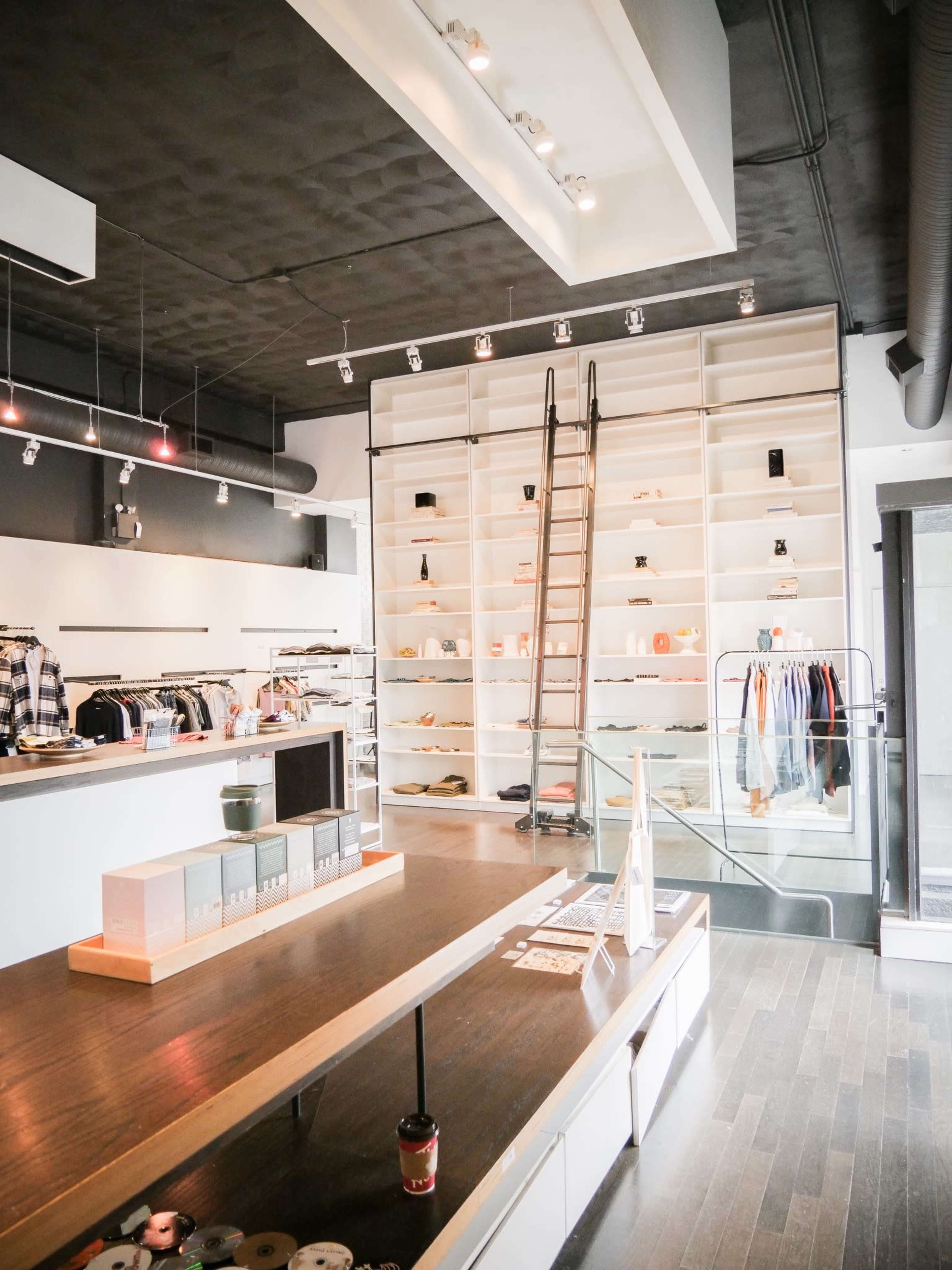A modern retail store with clothing displays and a ladder against a shelf filled with merchandise.