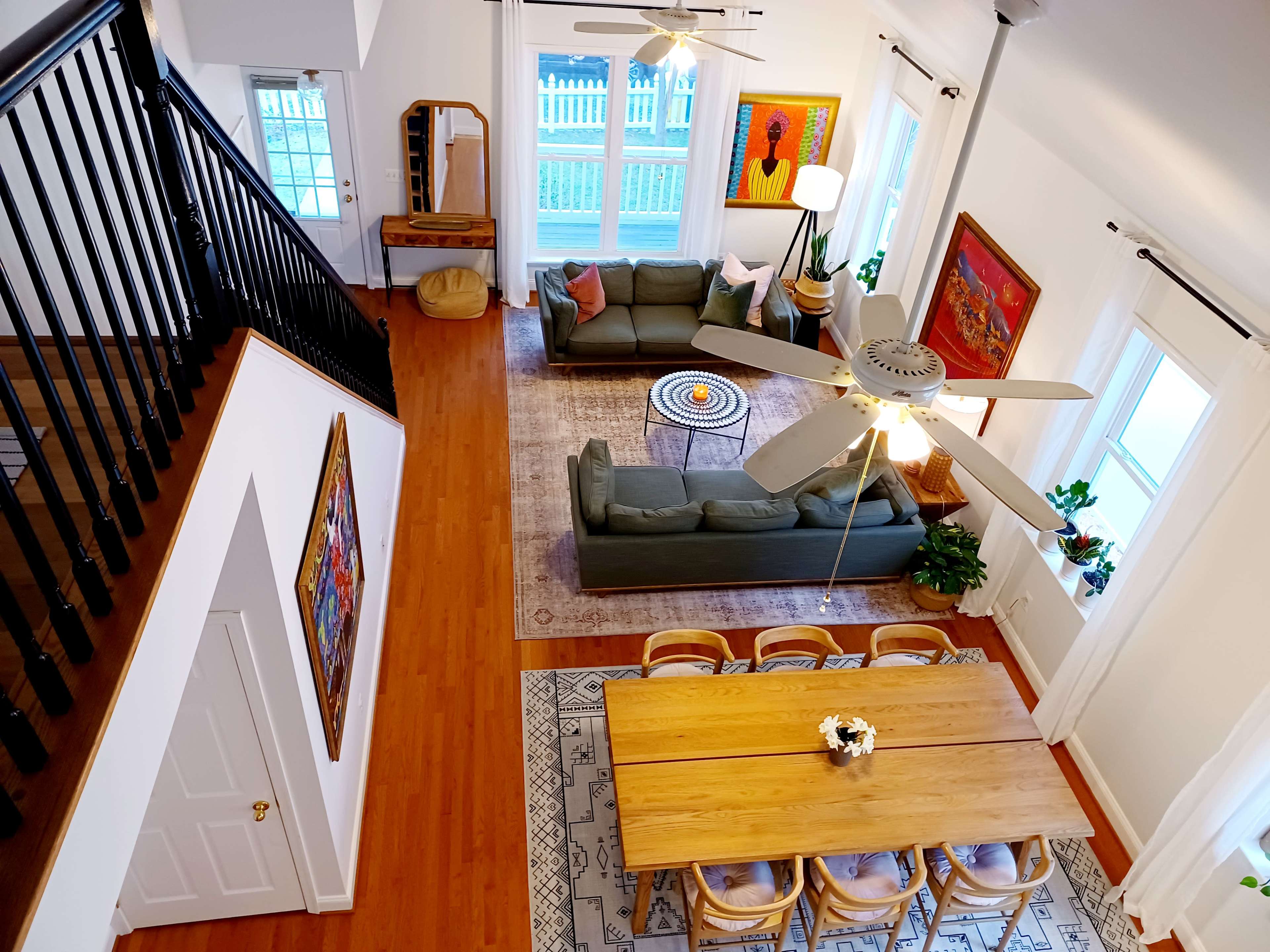 A well-lit, two-story living space with a green sofa, wooden dining table, and decorative art on the walls.