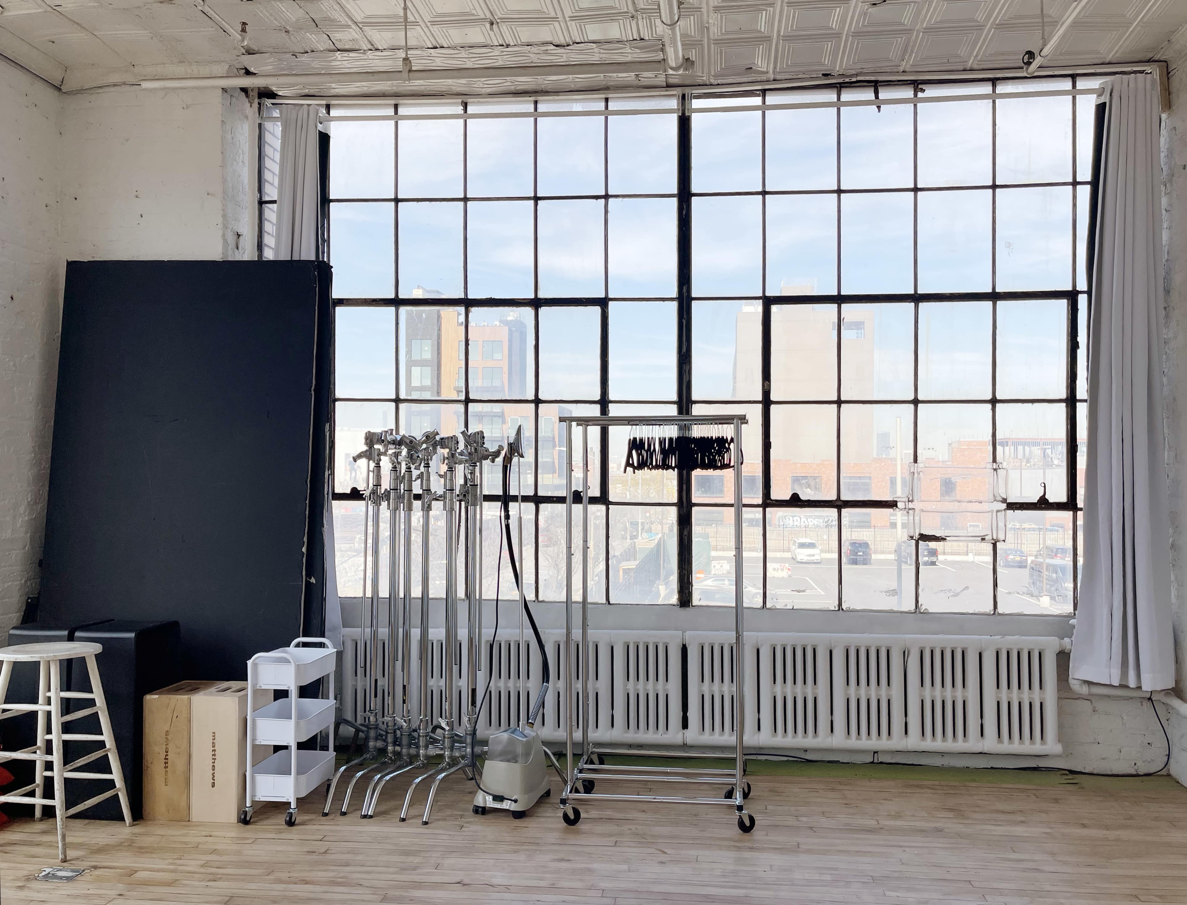 A spacious studio with large windows, a simple white backdrop, and equipment racks against a bright, urban backdrop.