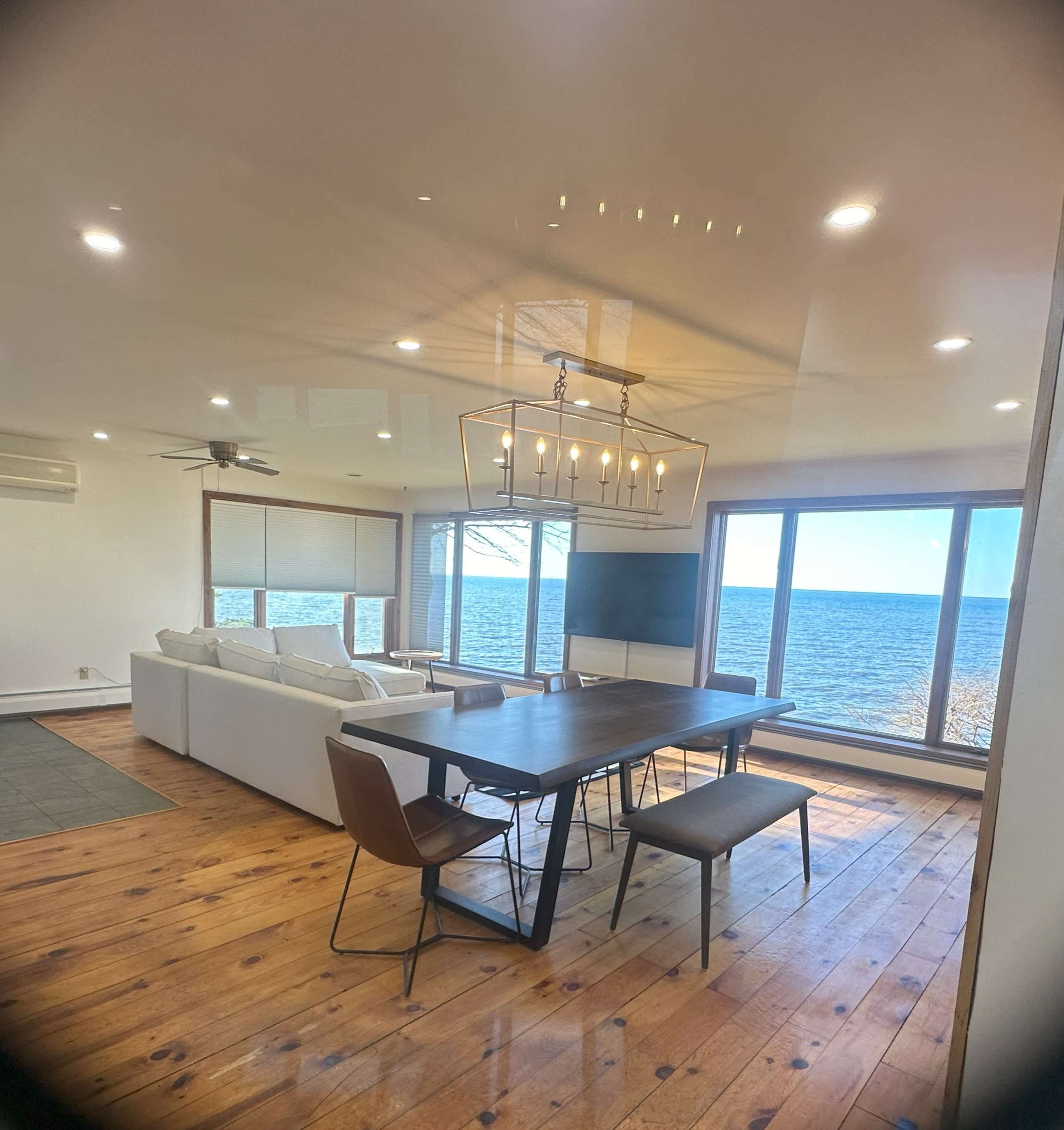 A dining area with a wooden table and chairs overlooks a large window displaying a view of the water.
