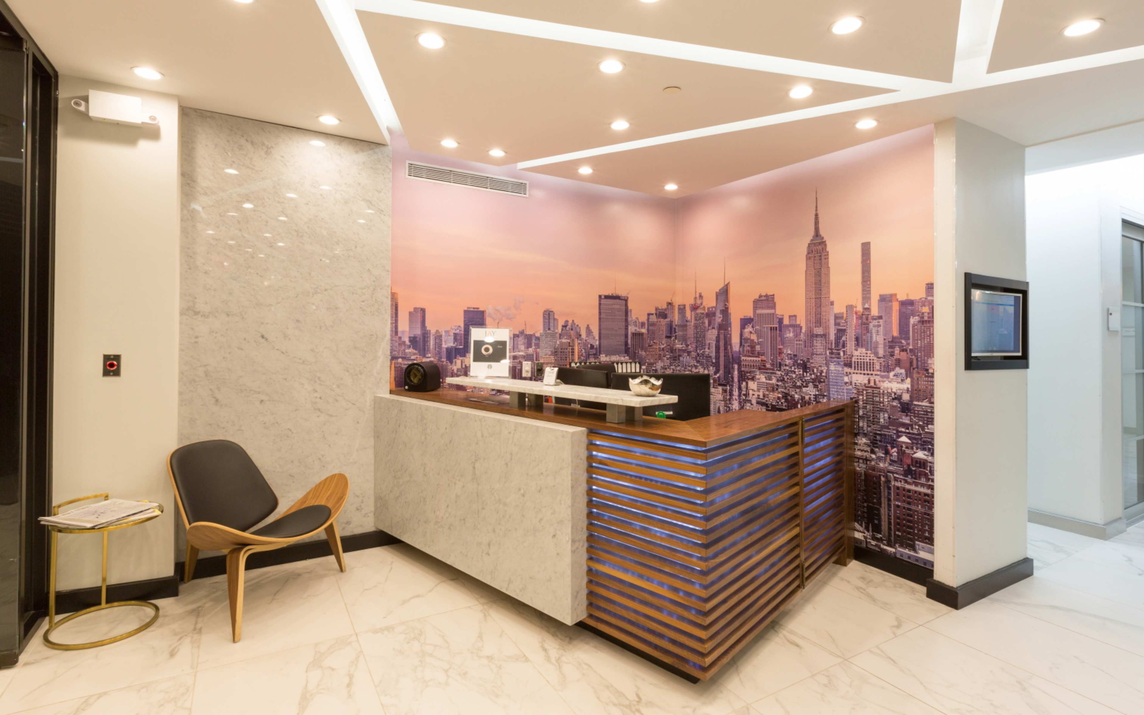 The image shows a modern reception area with a wooden front desk, a city skyline mural, and contemporary seating.
