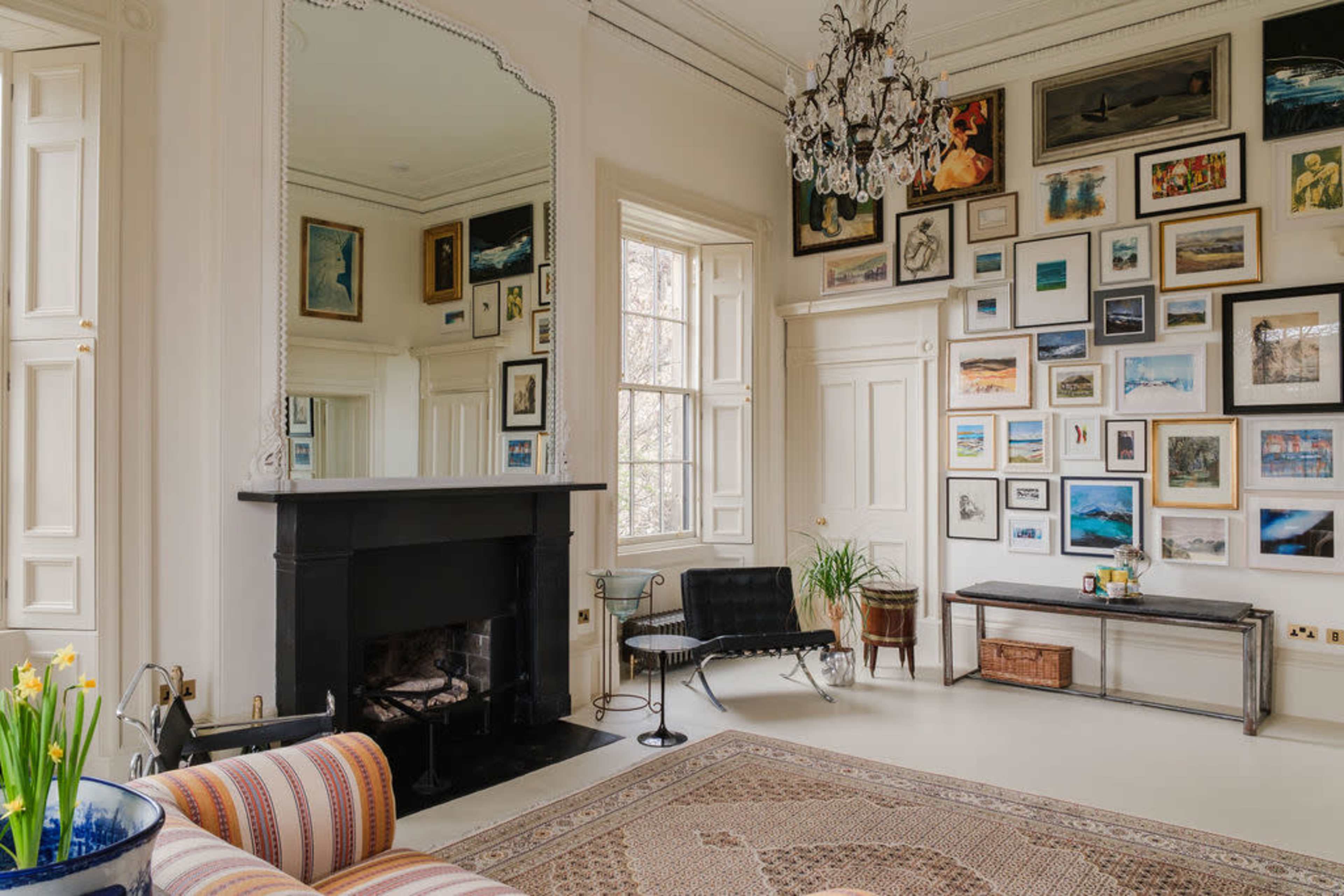 The room features a black fireplace, a large mirror, and a wall adorned with a variety of framed artworks and photographs.