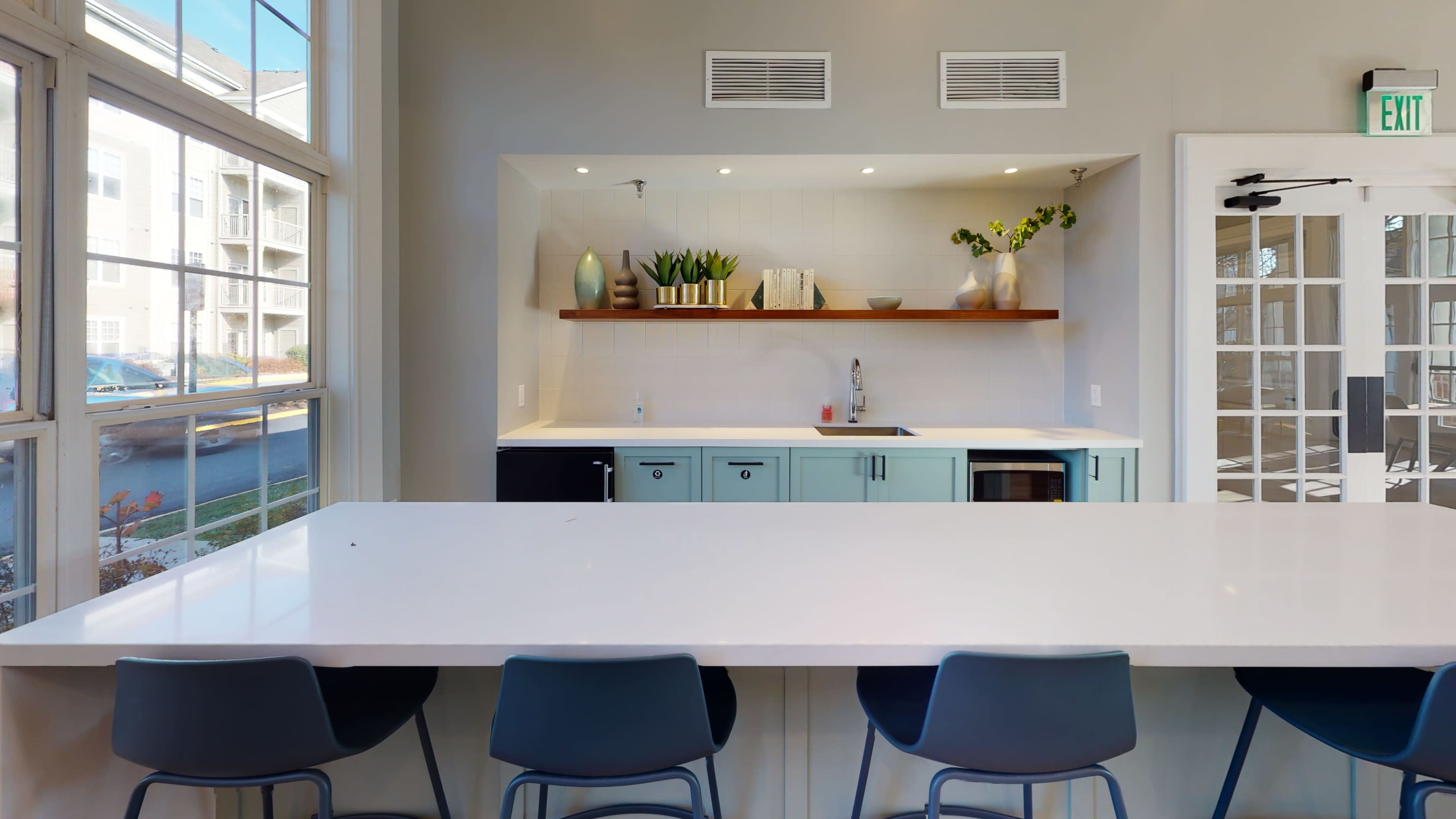 The image shows a modern kitchen with light blue cabinets, a white countertop, and a shelf adorned with plants and decorative items.