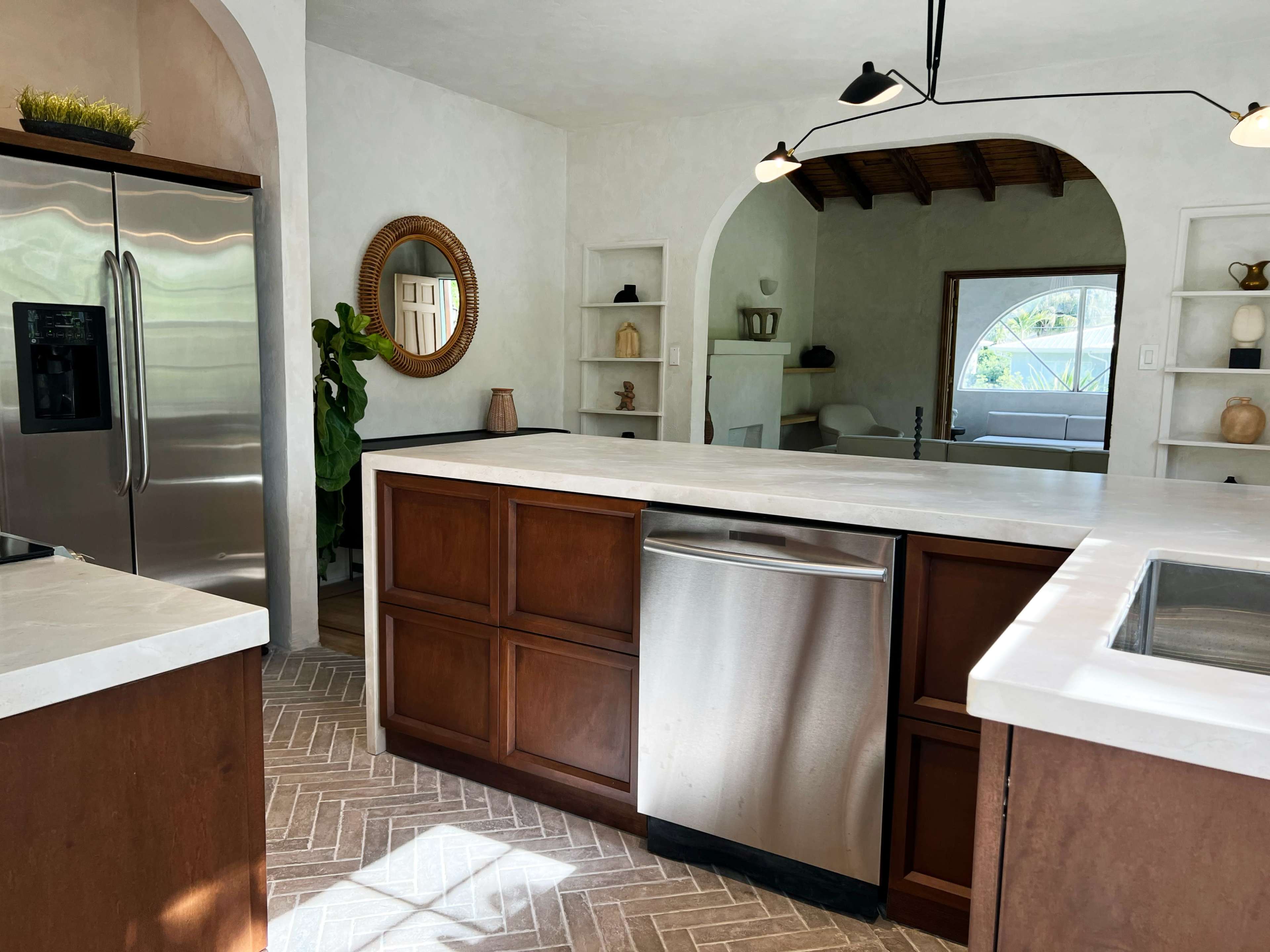 The image shows a modern kitchen with wooden cabinets, stainless steel appliances, and a large island featuring a light-colored countertop.