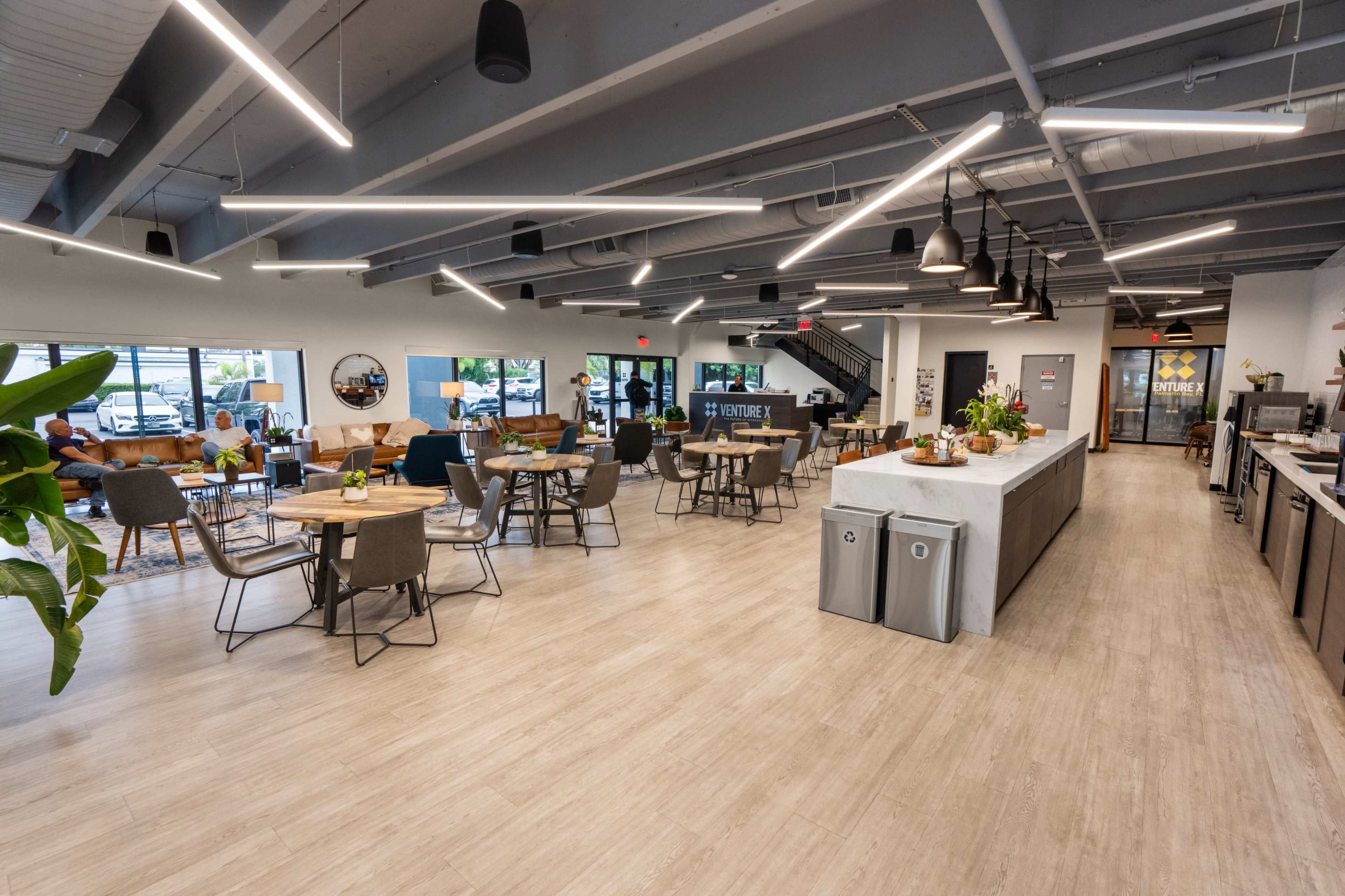 The image shows a spacious, modern café with tables, chairs, and a serving area, featuring a well-lit interior and large windows.