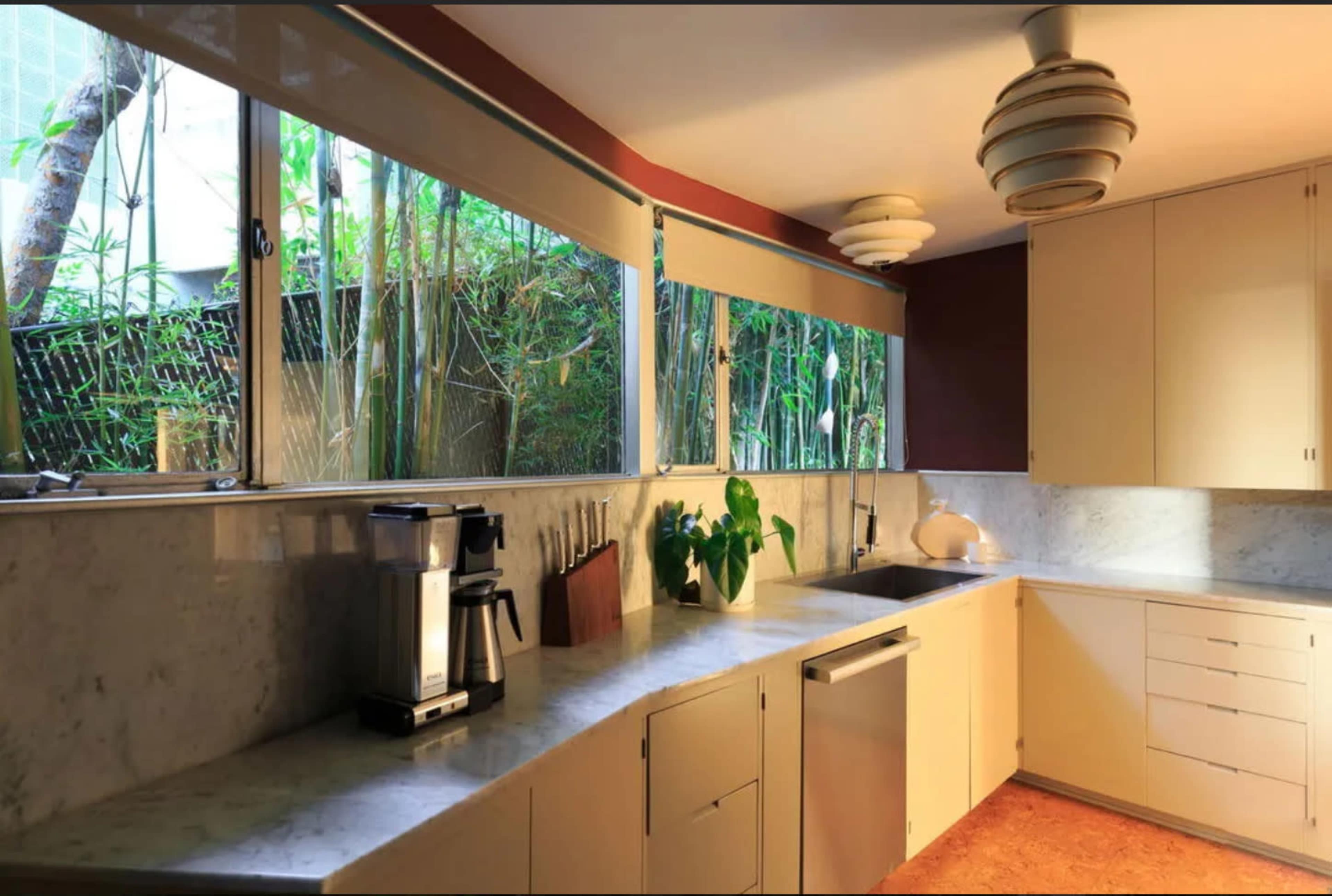 A modern kitchen features a marble countertop, stainless steel appliances, and large windows overlooking a green garden.