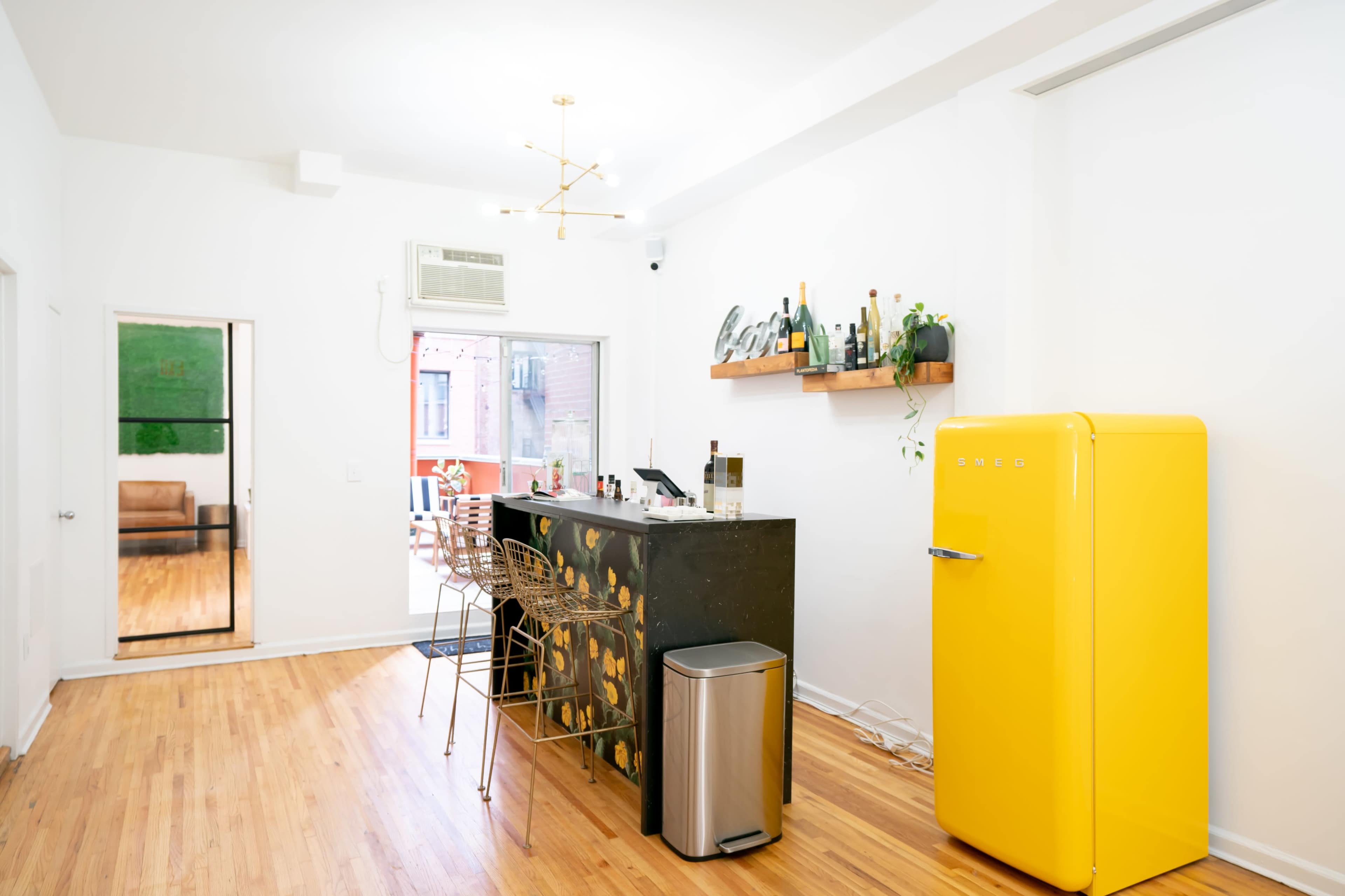 A bright kitchen with a yellow refrigerator, a bar counter adorned with plants, and wooden flooring.