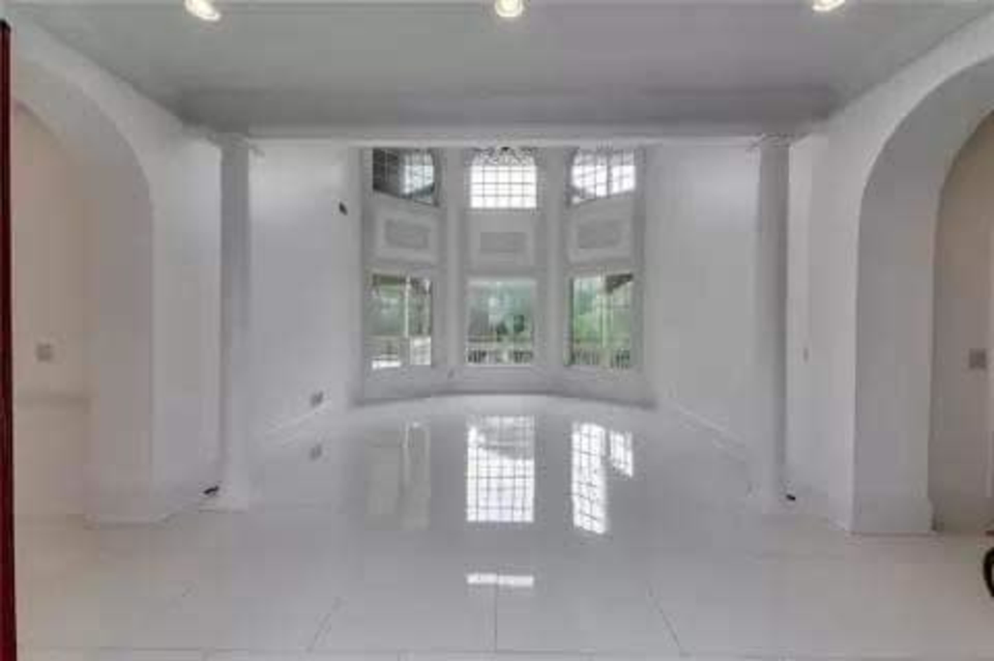 A spacious, empty room with large windows and glossy white tiled floors.