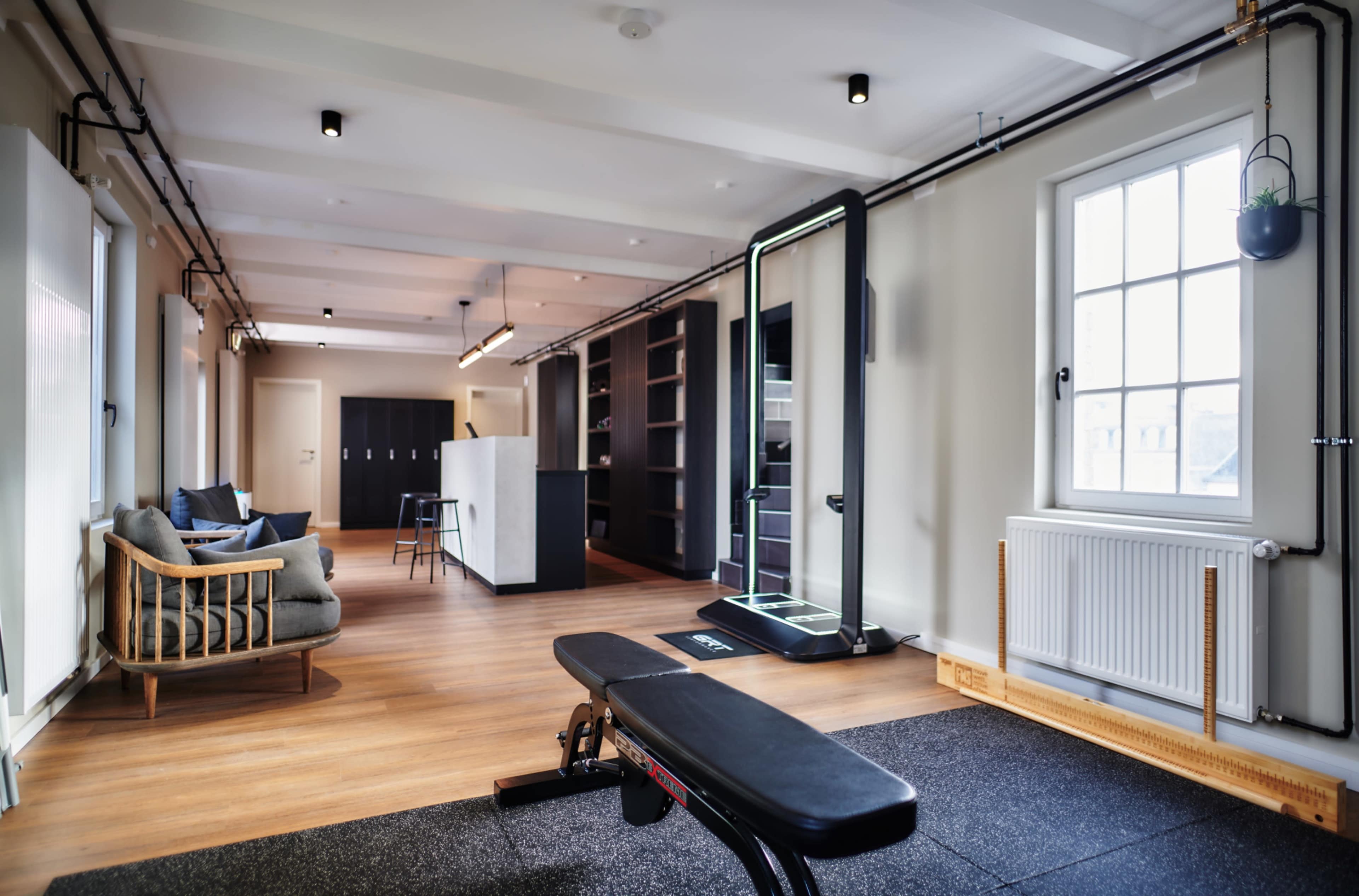 The image shows a spacious, modern home gym with exercise equipment, a comfortable seating area, and large windows.