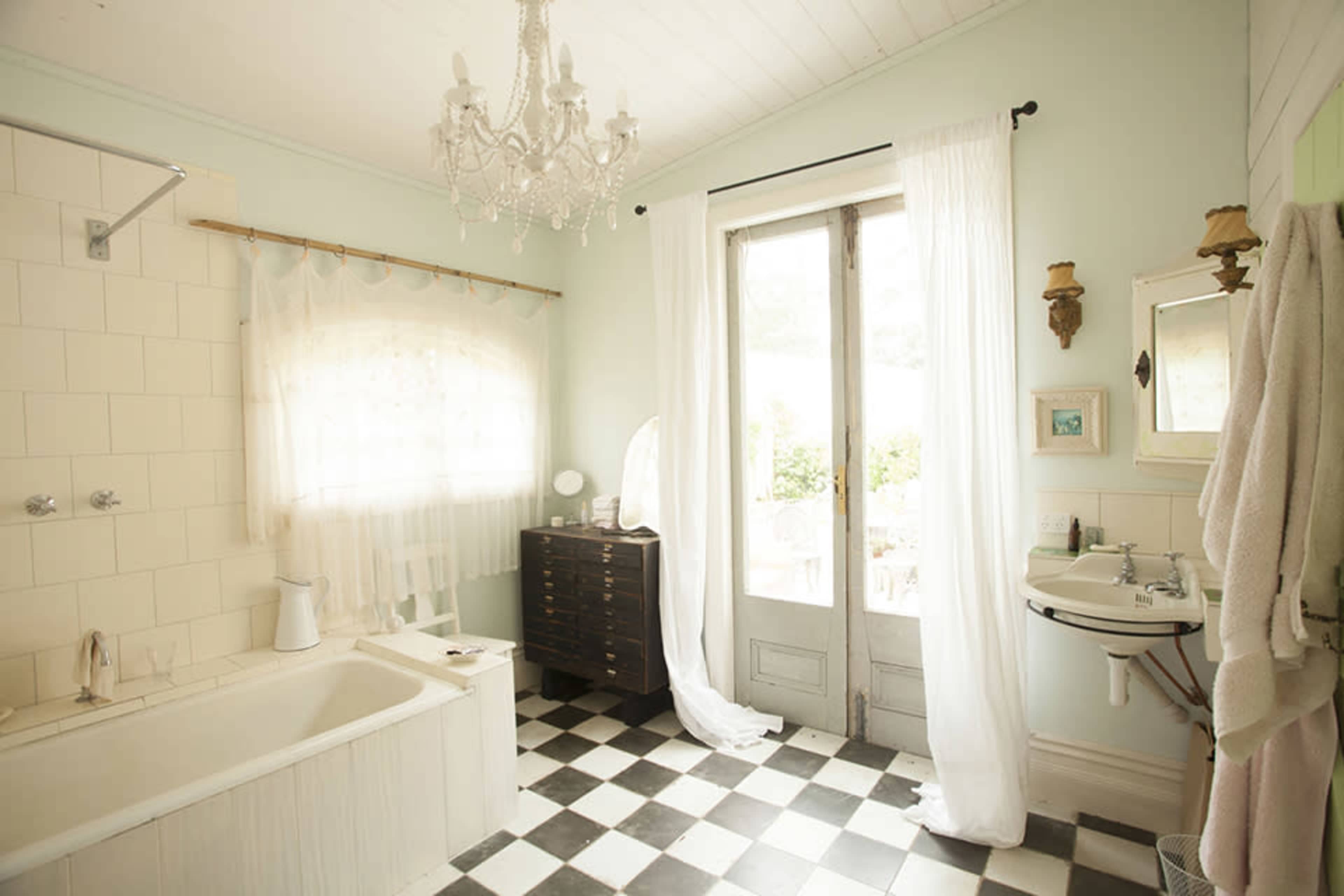 The bathroom features a white bathtub, a checkered black-and-white floor, and large windows draped with sheer curtains.