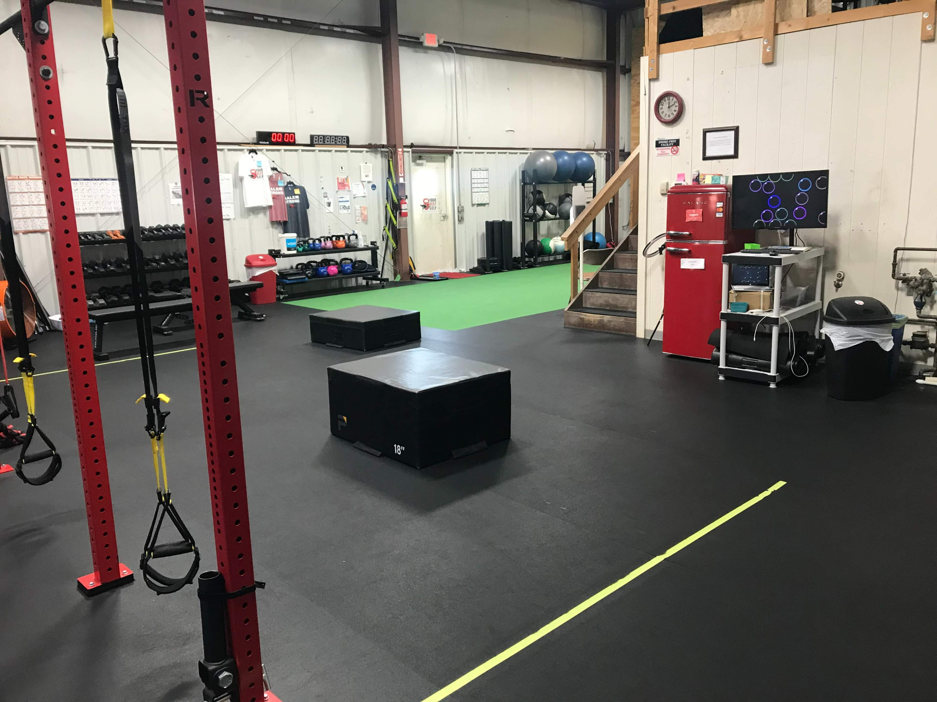 A gym interior featuring suspension training equipment, a few black boxes for exercises, and various workout stations with weights and exercise equipment.