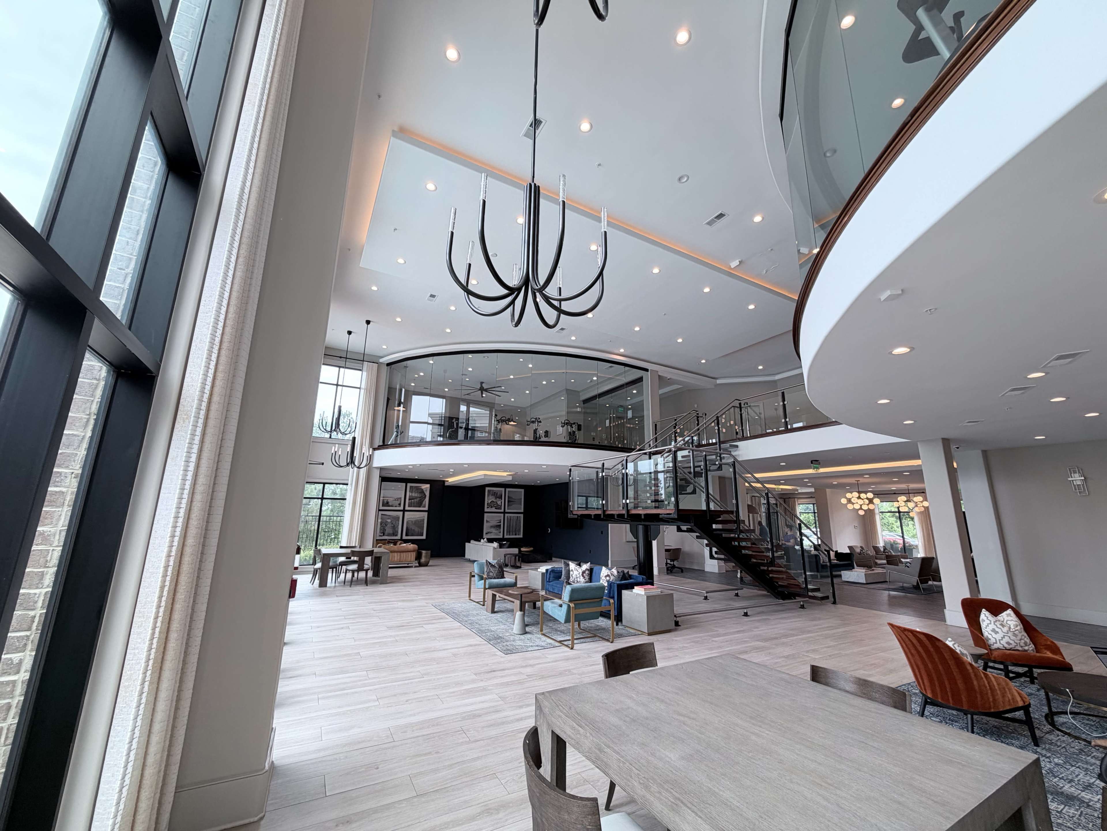 The image shows a spacious, modern interior of a multi-level living area with large windows, elegant furnishings, and a staircase leading to an upper level.