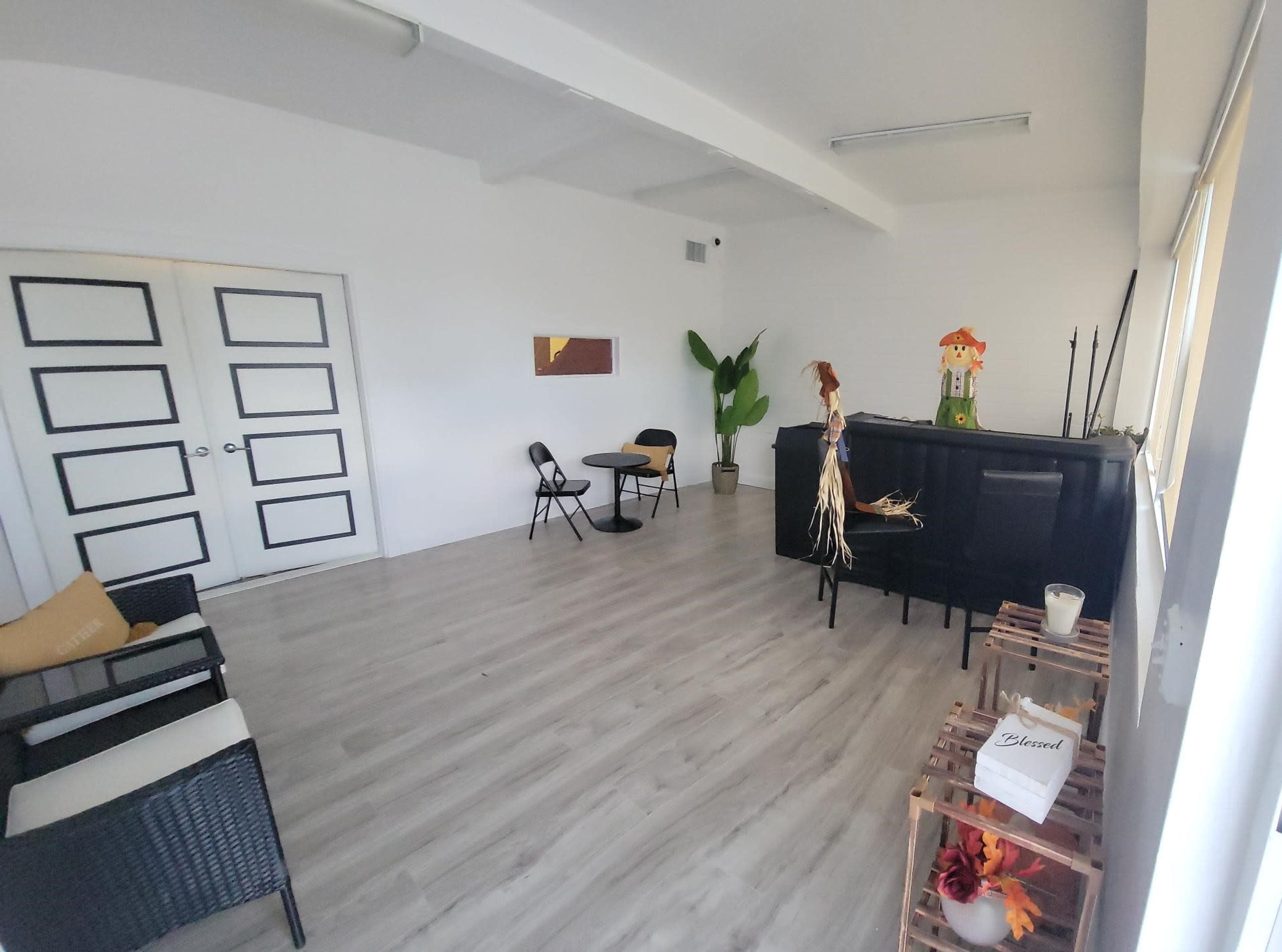 A sparsely furnished room with a black counter, a small table and chair, and a potted plant against white walls.
