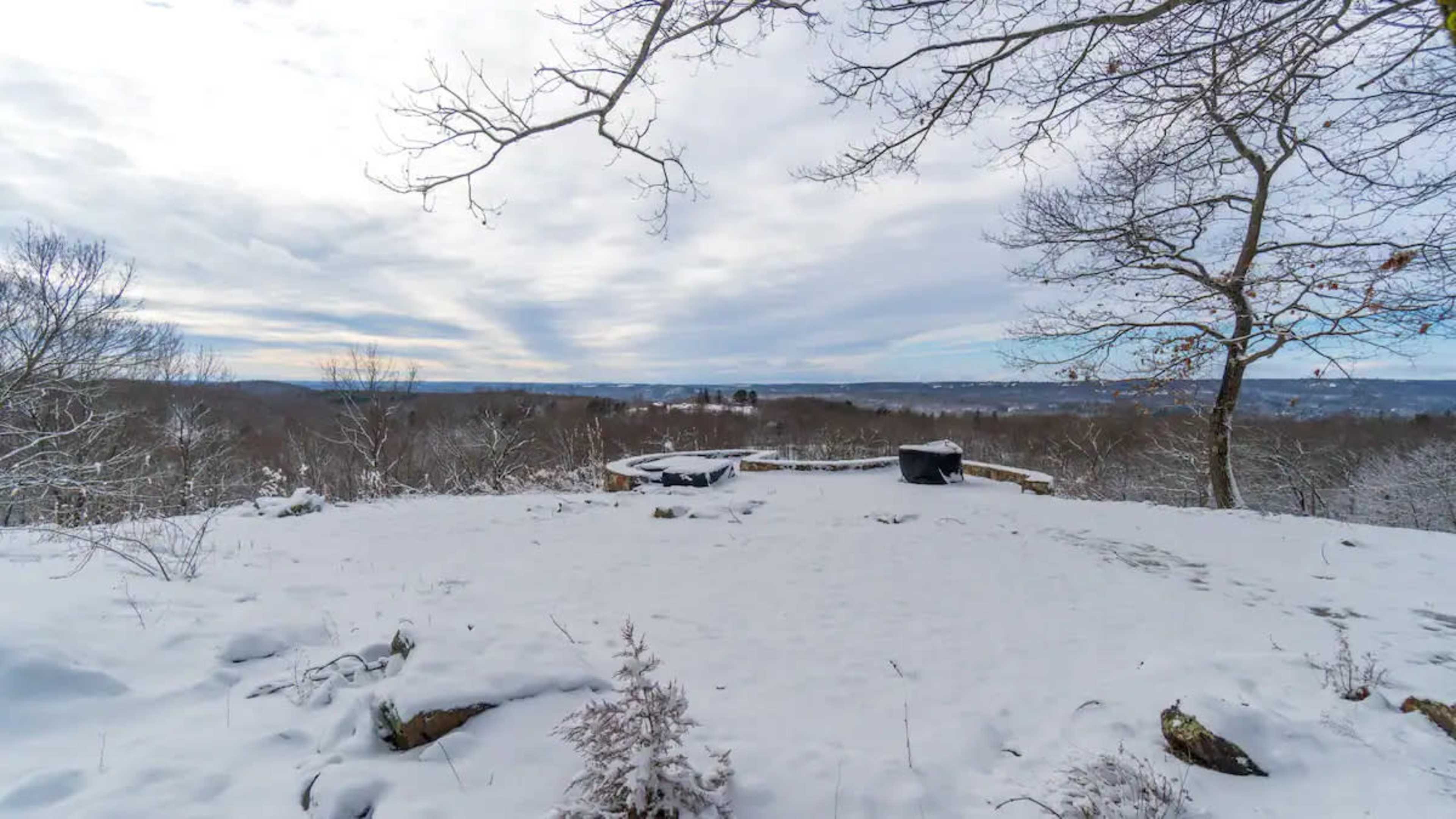 A snowy landscape with a circular stone patio overlooking a valley under a cloudy sky.