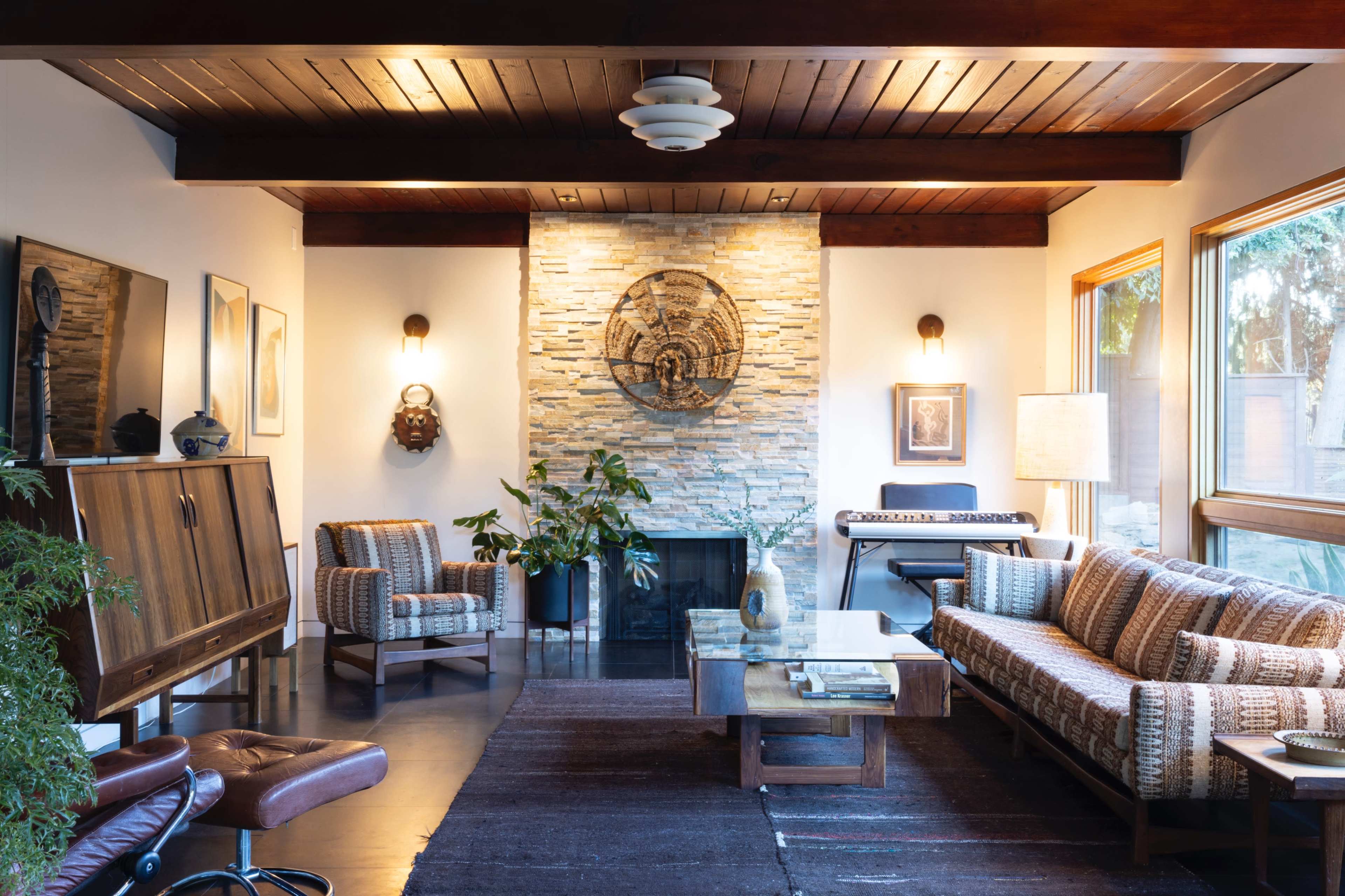 A modern living room featuring a stone fireplace, wooden beams, and various seating options, including a patterned couch and armchairs.