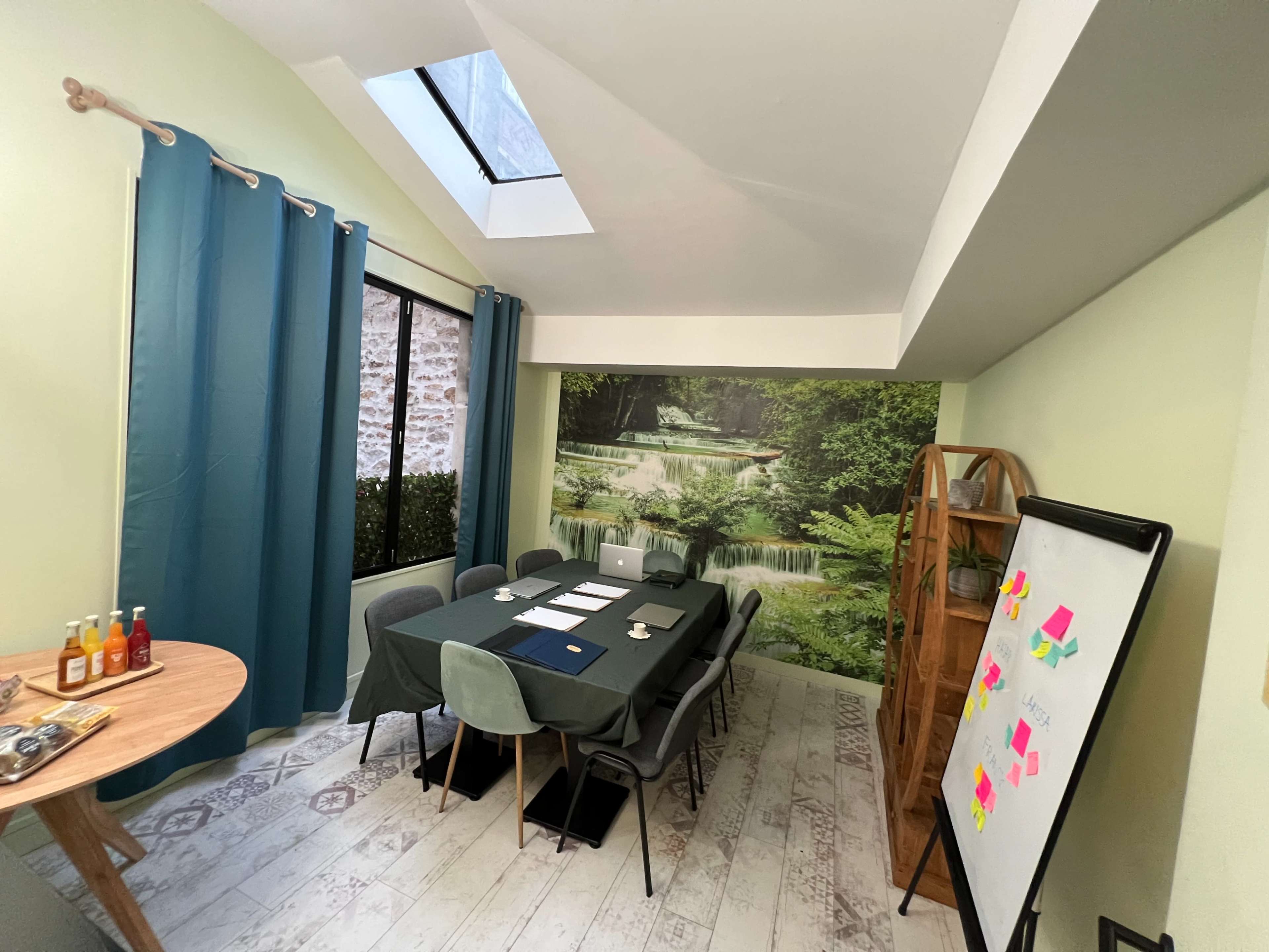 A meeting room features a large table surrounded by chairs, with a mural of a serene landscape, a whiteboard, and a window above.
