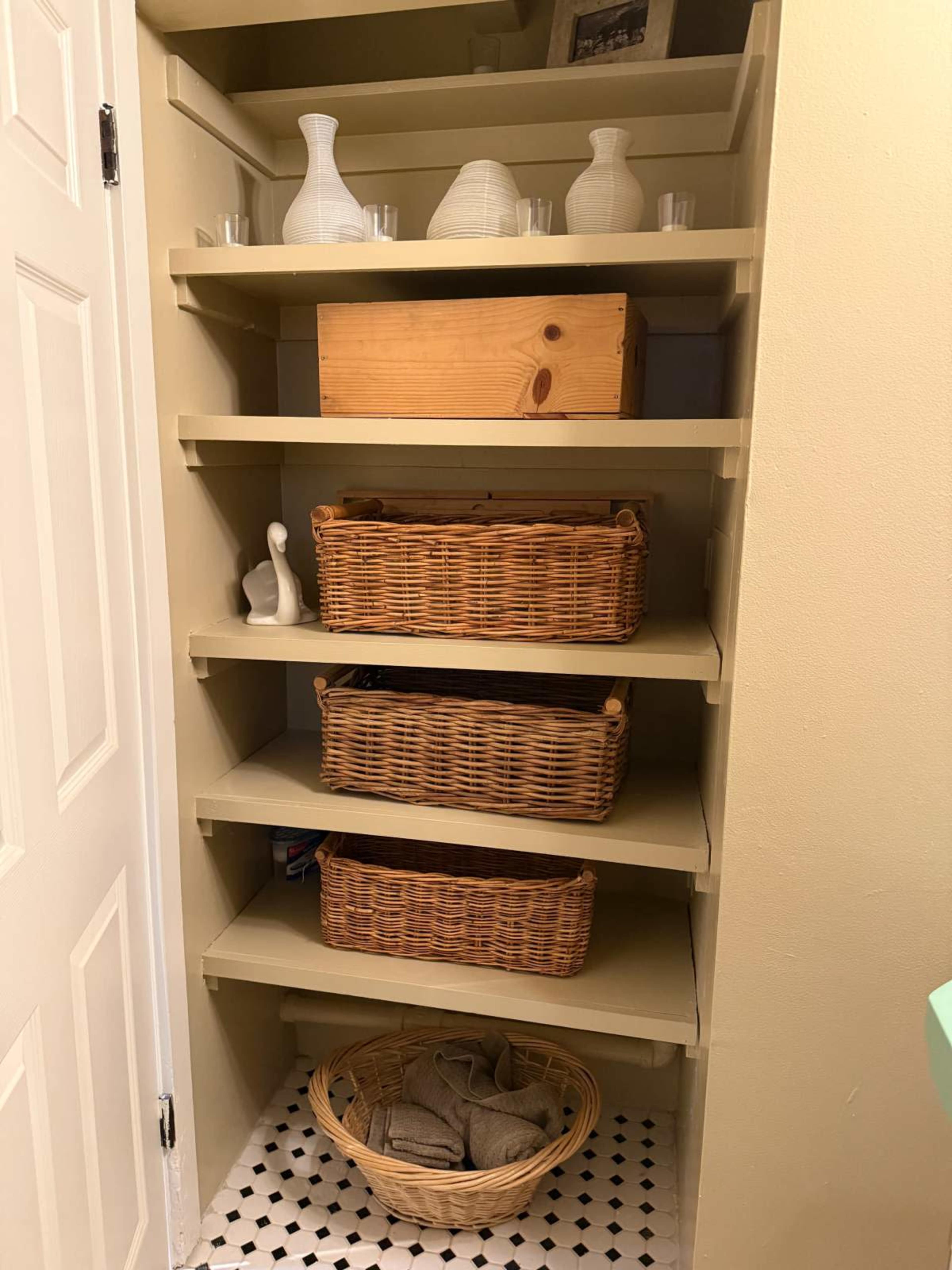 The image shows a staircase leading into a storage closet featuring several shelves filled with woven baskets, decorative items, and a wooden box.