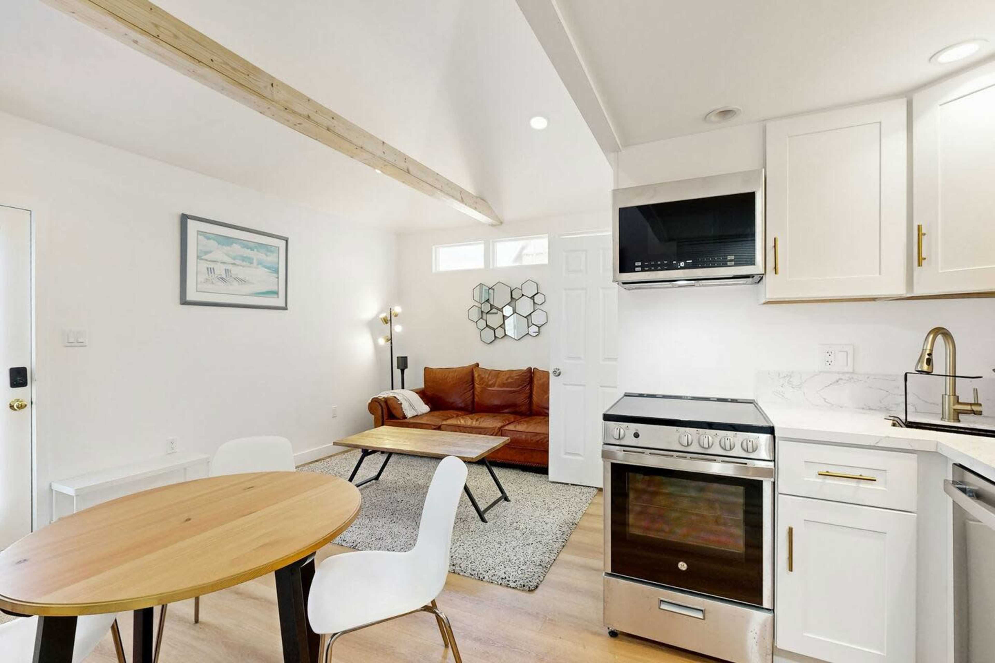 A small, modern kitchen with a dining table, a living area featuring a brown sofa, and a door leading outside.