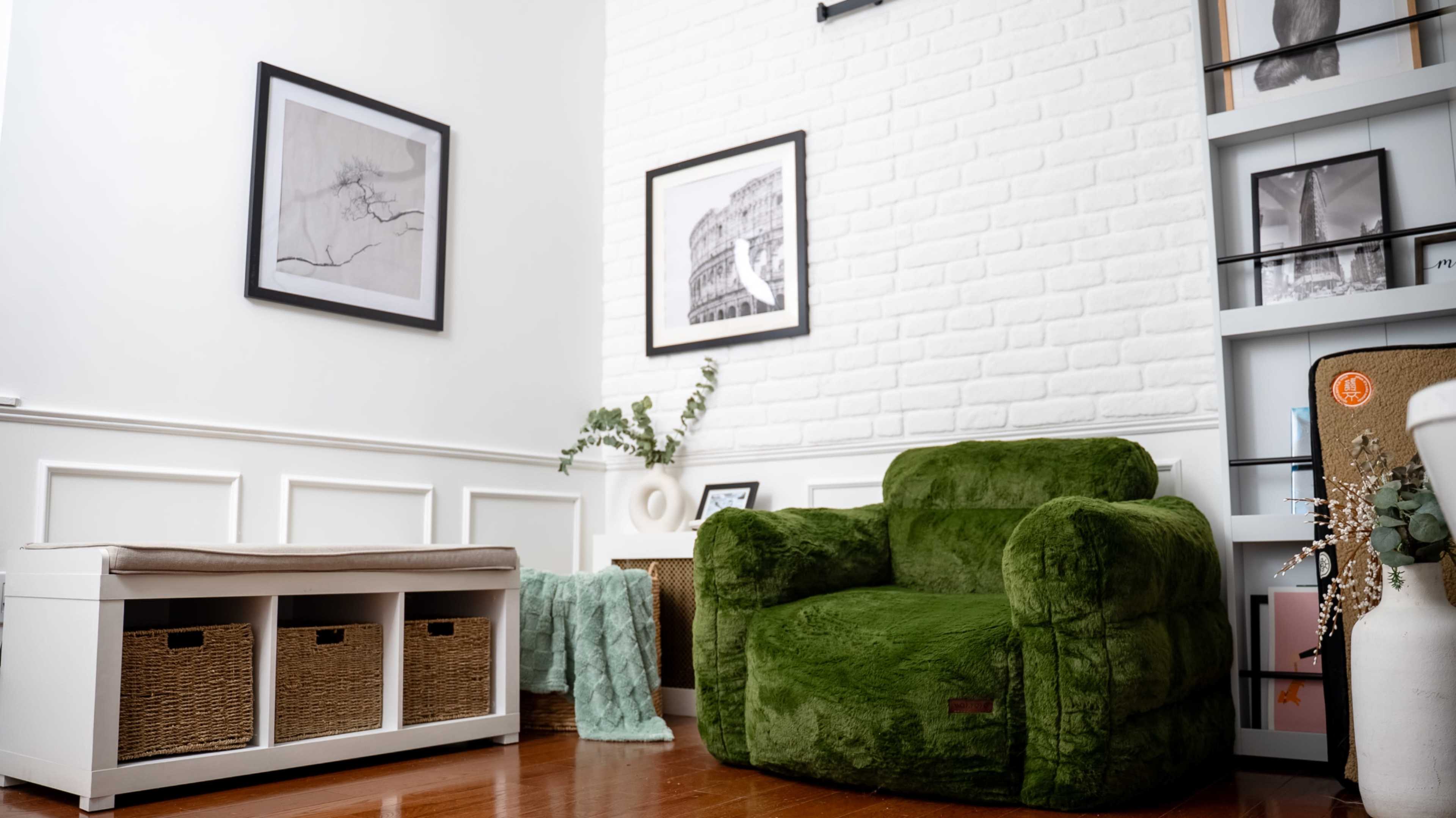 The scene features a cozy room with a green armchair, framed artwork on the walls, and a storage bench with woven baskets.