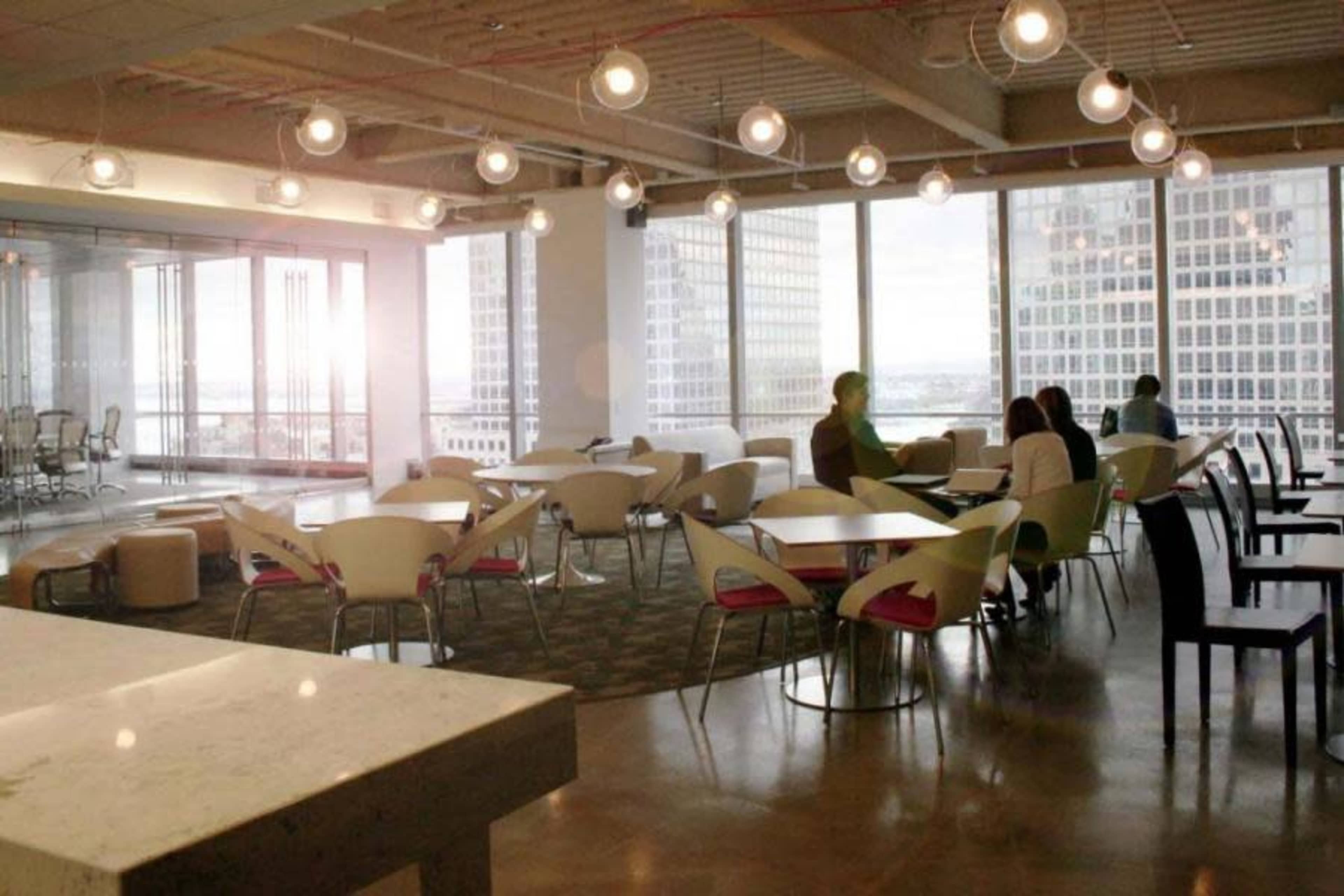 A spacious office break area with modern furniture, large windows, and pendant lighting.