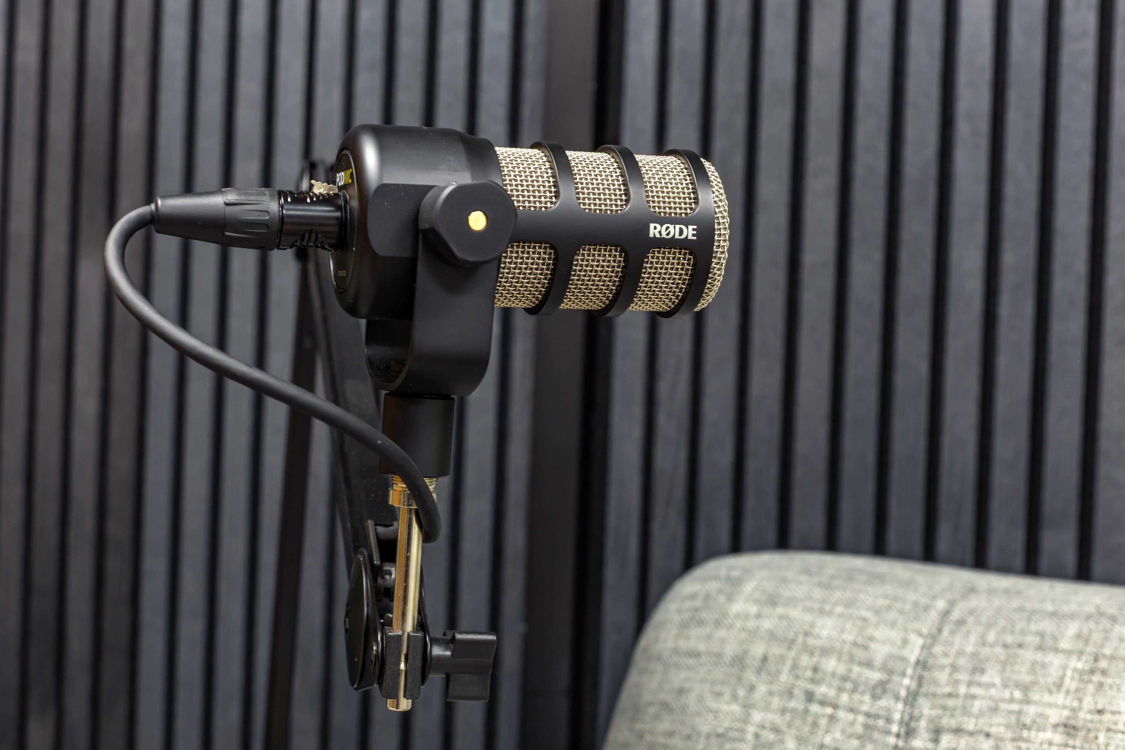 The image shows a Rode microphone mounted on a stand with a textured black background.