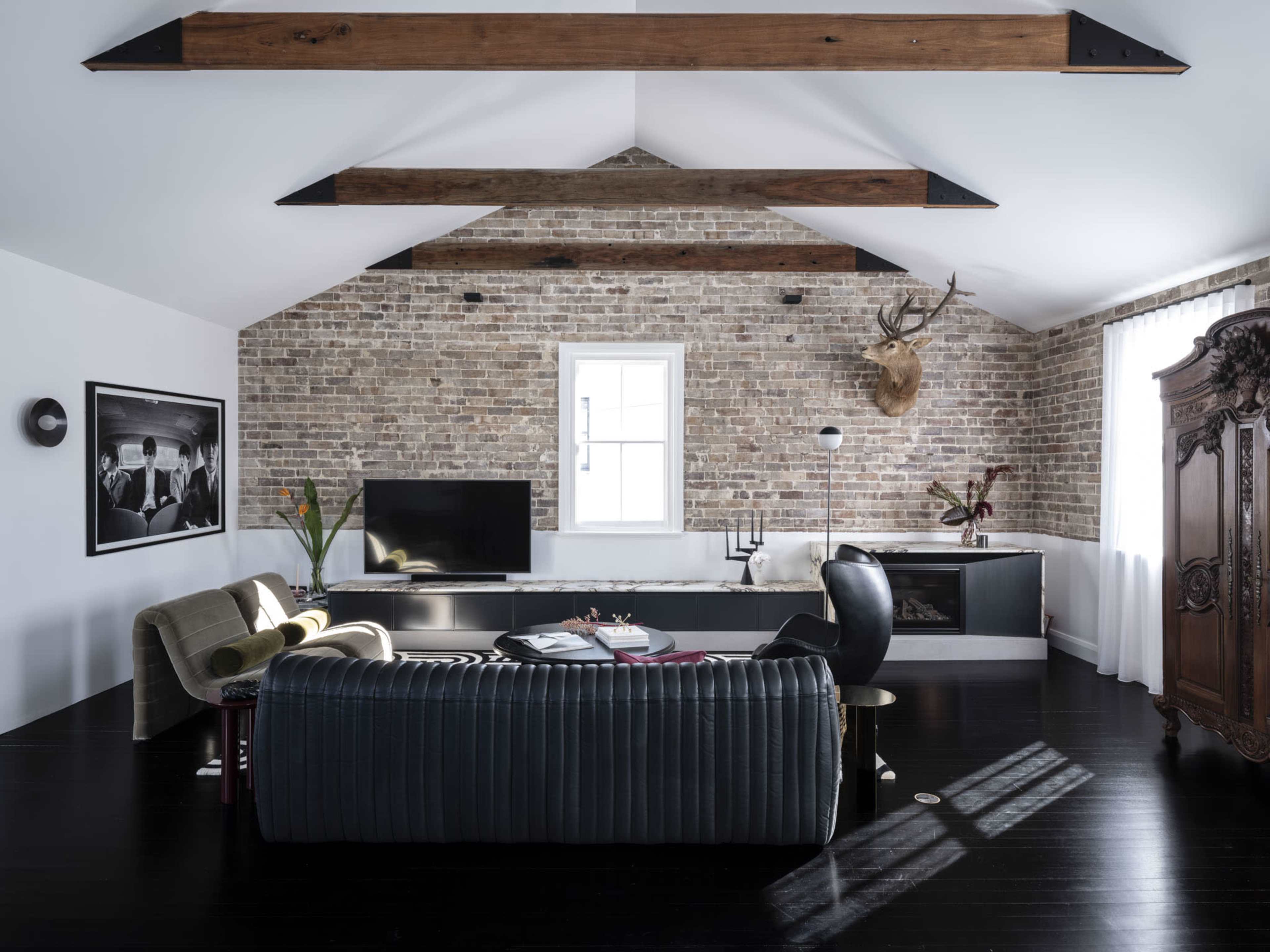The living room features a combination of exposed brick walls, wooden beams, and modern furniture, including a sofa and a television unit.