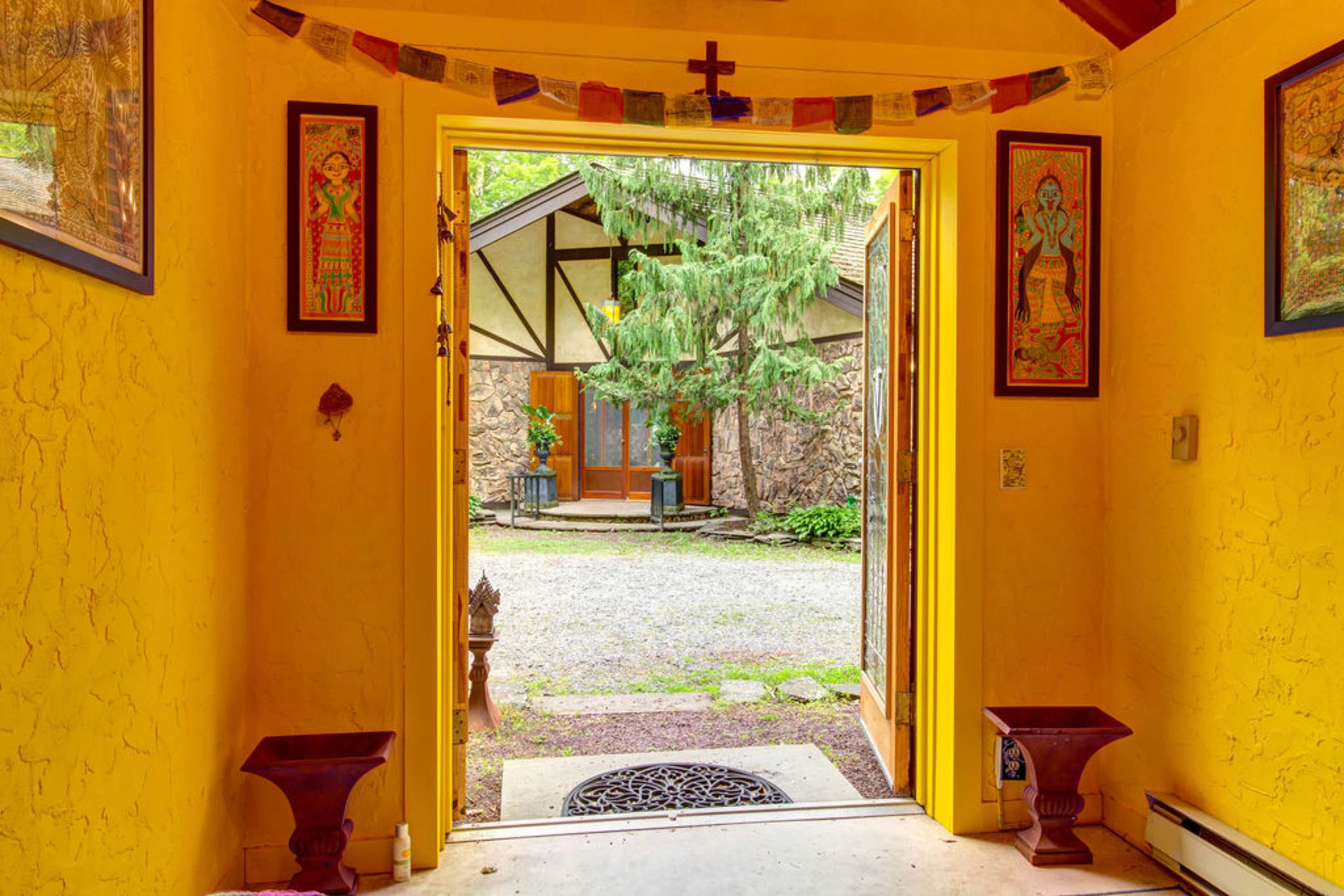 A yellow-walled entrance leading to a gravel courtyard, framed by artwork and decorative items on either side.