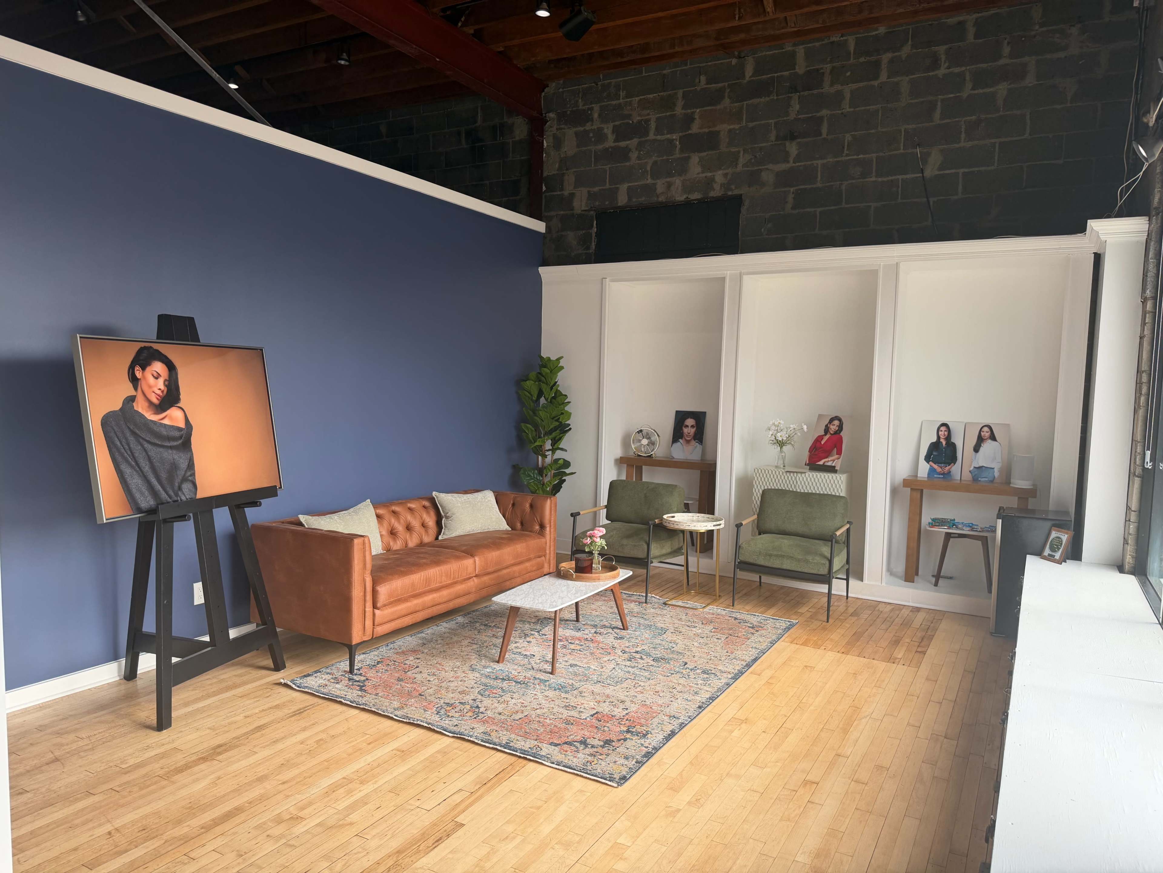 The image shows an interior space featuring a brown leather sofa, a blue accent wall, and several portraits displayed on shelves.