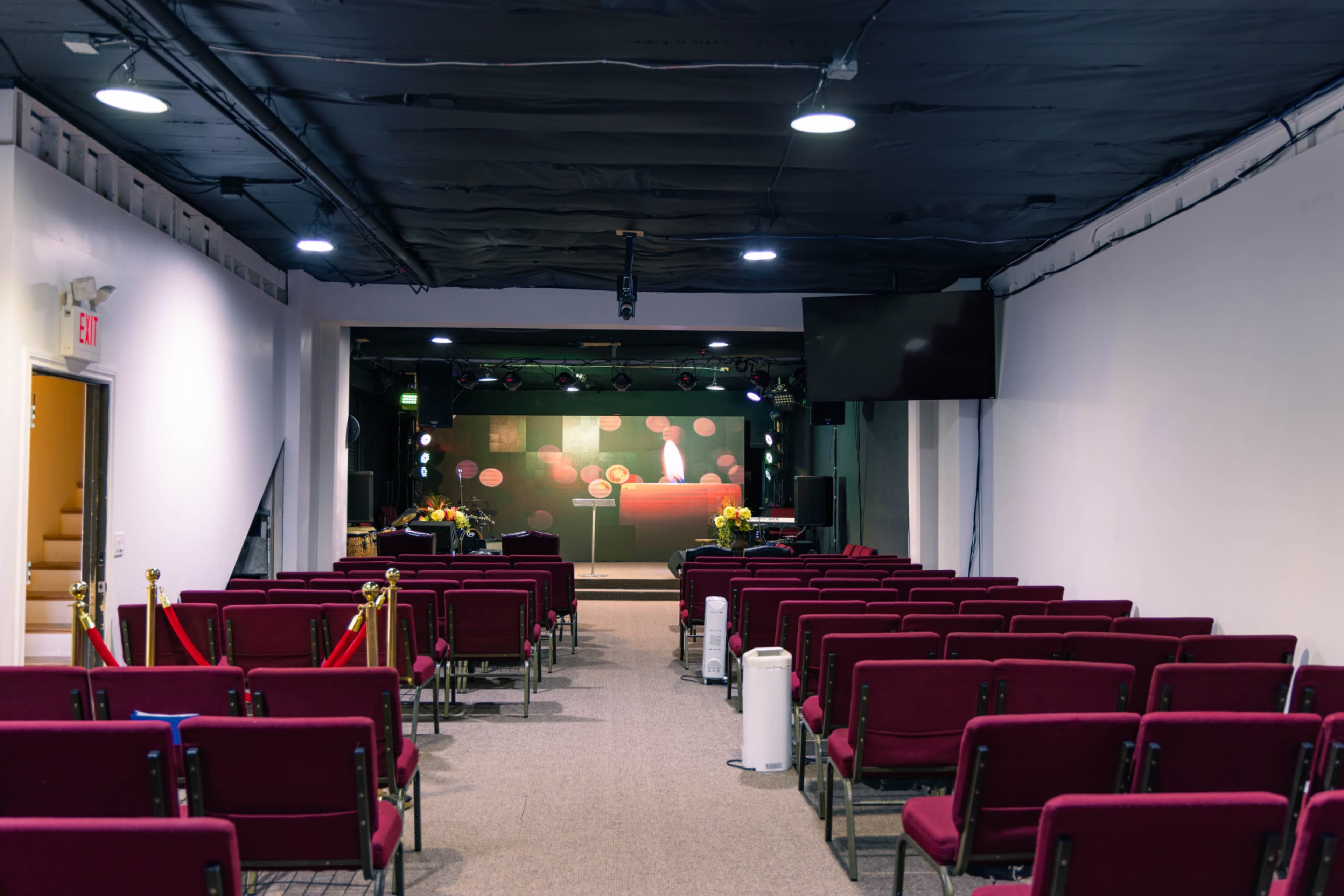 A theater-style room is set up with rows of burgundy chairs facing a stage adorned with screens and decorations.