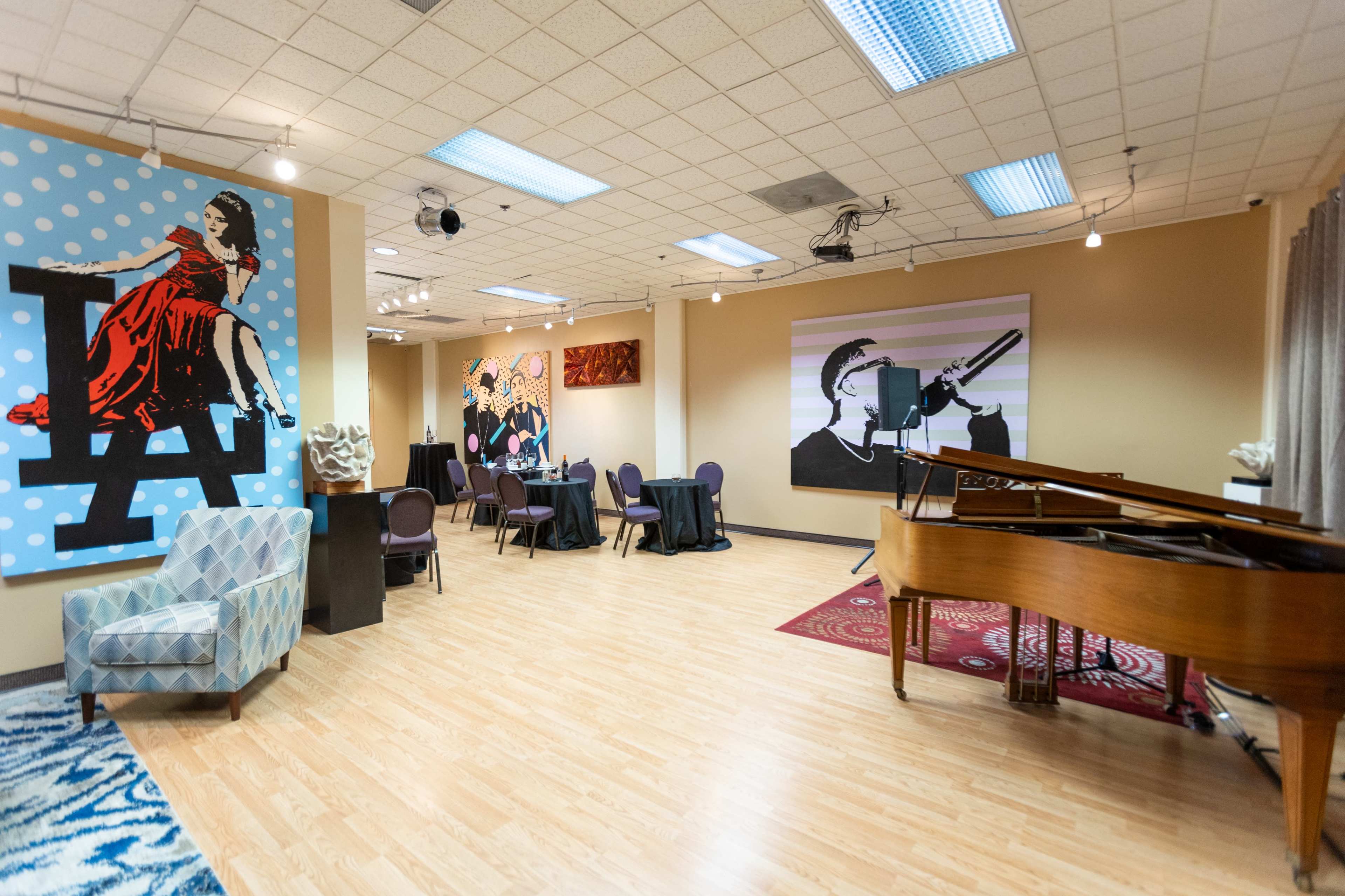 A spacious art-filled lounge with a piano, tables set for dining, and colorful murals on the walls.