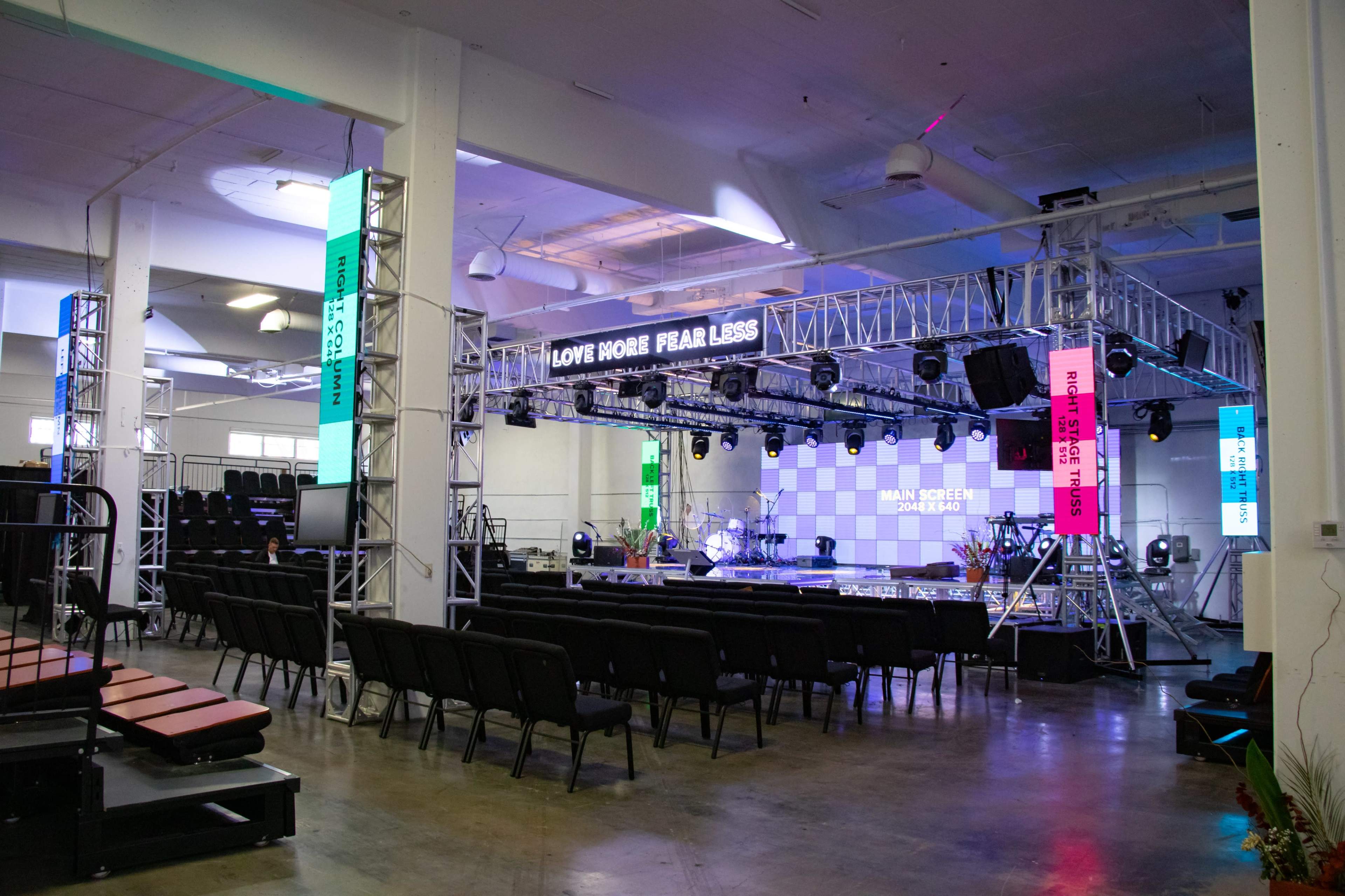 A spacious event venue set up with a stage, seating arrangements, and colorful lighting fixtures.