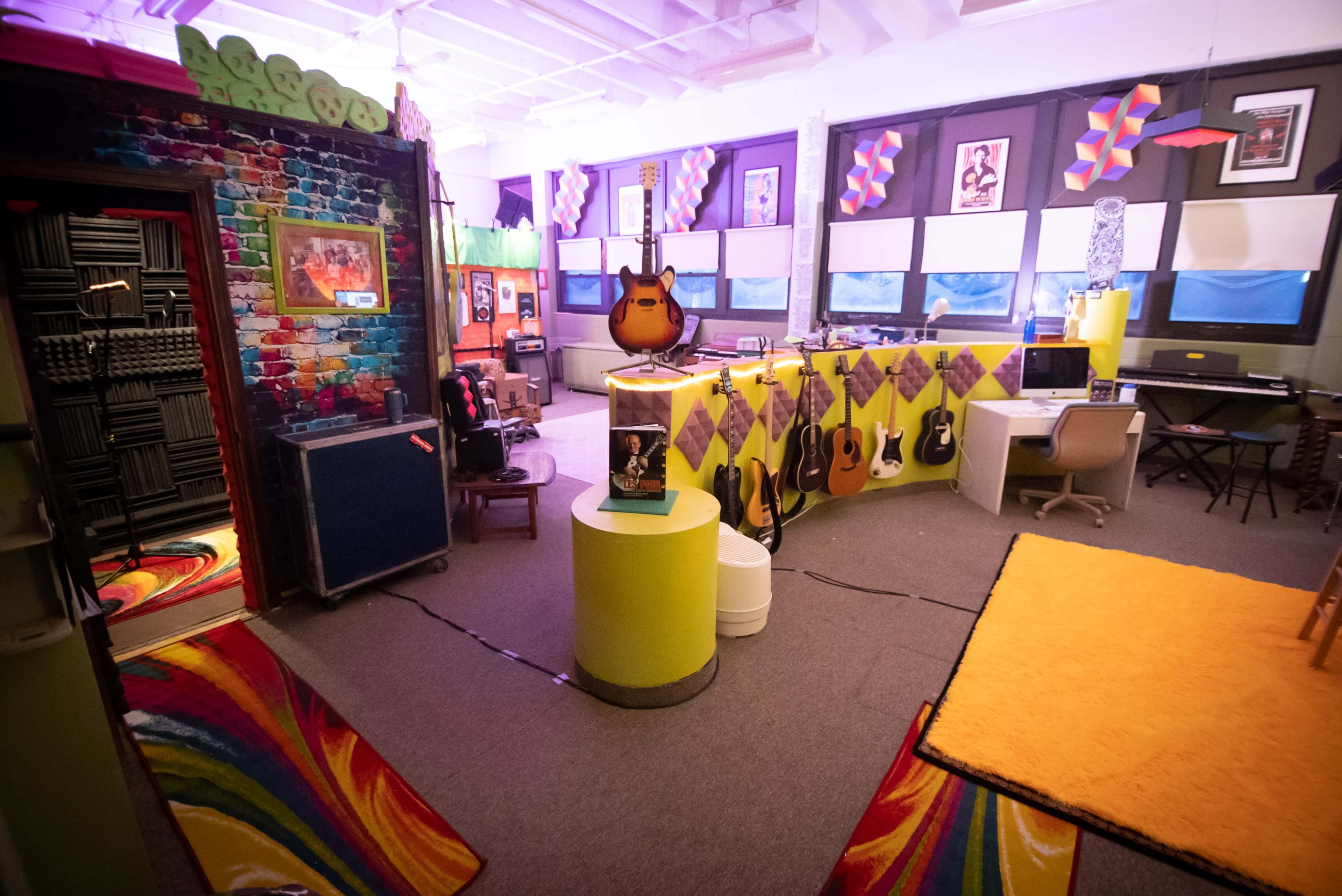 A vibrant music room featuring colorful walls, various guitars on display, soundproofing panels, and a recording area with a computer setup.